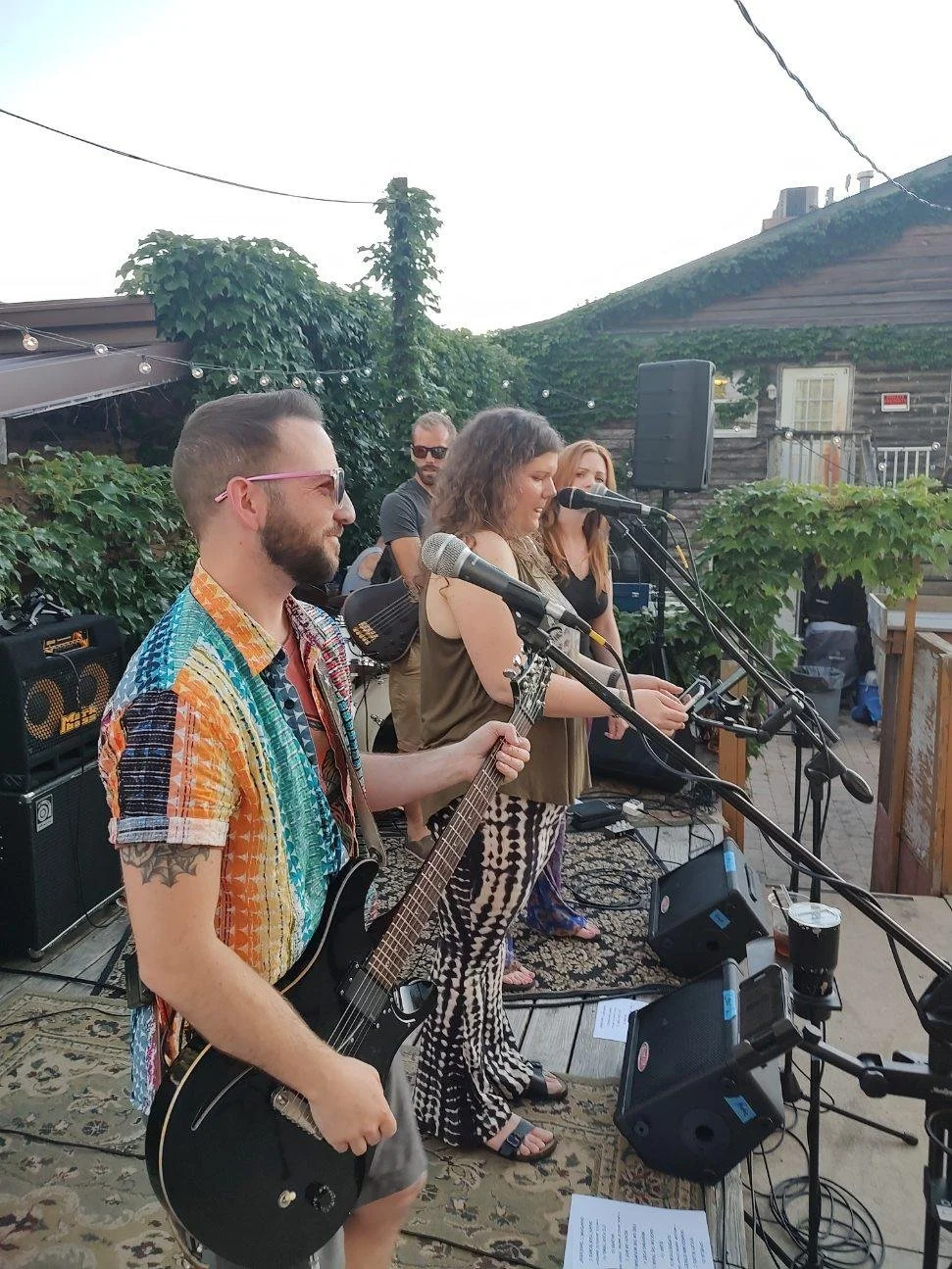 Live band performing outdoors with guitarist and singers in a garden setting.