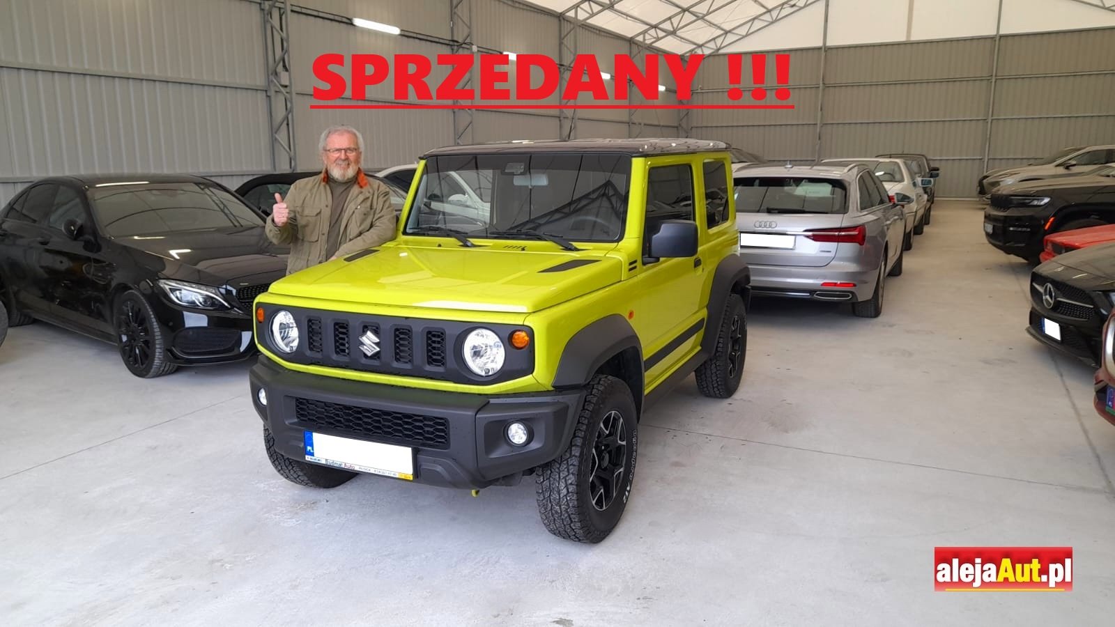 A bright yellow Suzuki Jimny SUV parked in an indoor showroom with several other cars around. A man with glasses, a beard, and a beige jacket is standing next to the vehicle, giving a thumbs up. Red text at the top says 'SPZEDANY!!!', and a URL 'alejaAut.pl' is at the bottom right corner.