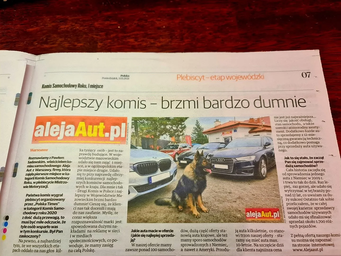 Polish newspaper article about car dealerships, featuring a photo of several luxury cars, including BMW, Audi, and Mercedes, parked outdoors with a German Shepherd dog sitting in front.