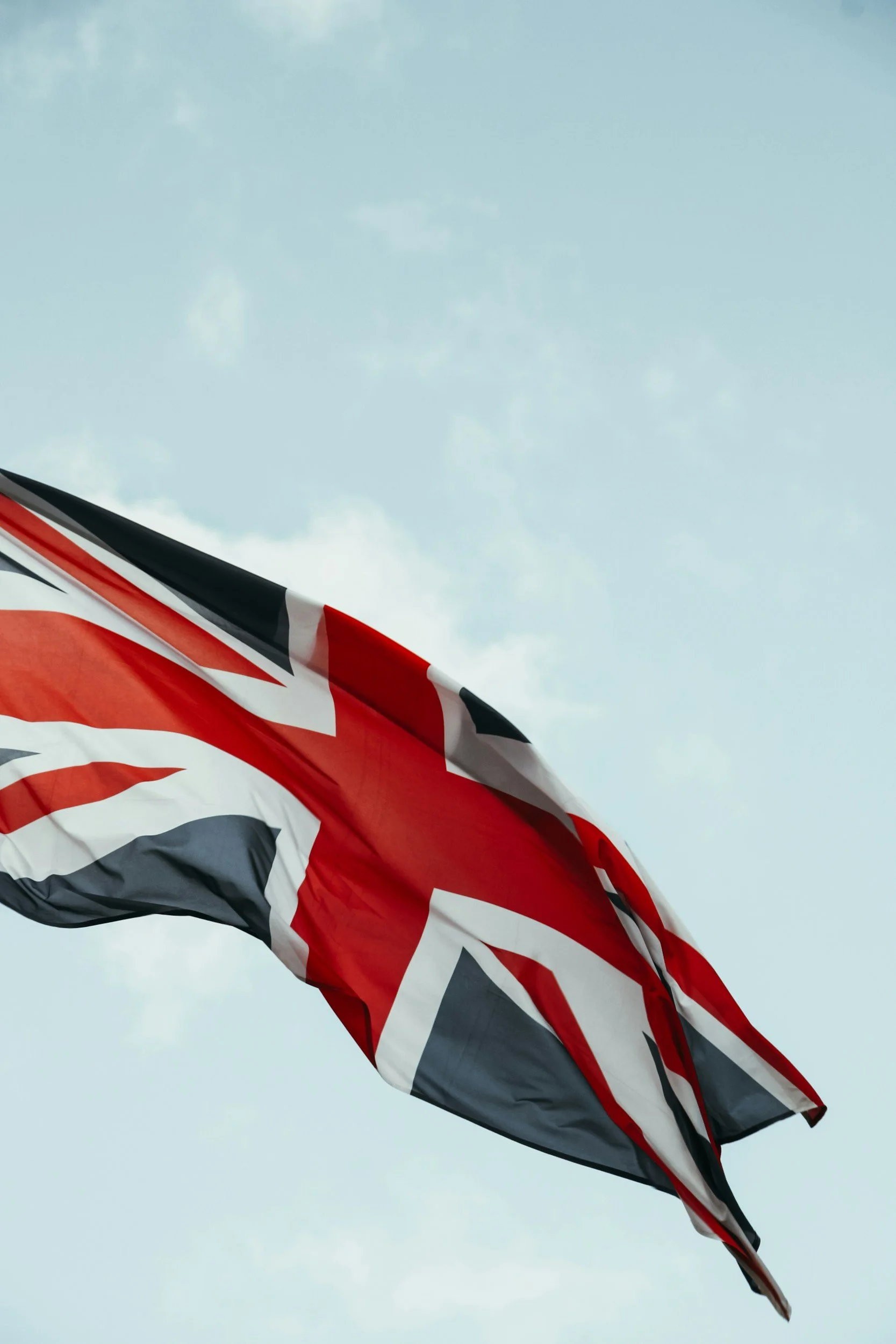 A flag with the Union Jack design flying against a cloudy sky.