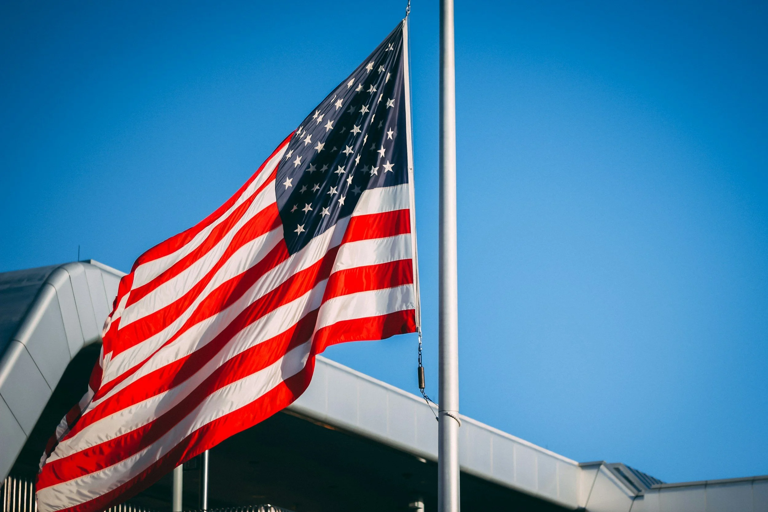 American flag flying outside on a sunny day with clear blue sky.