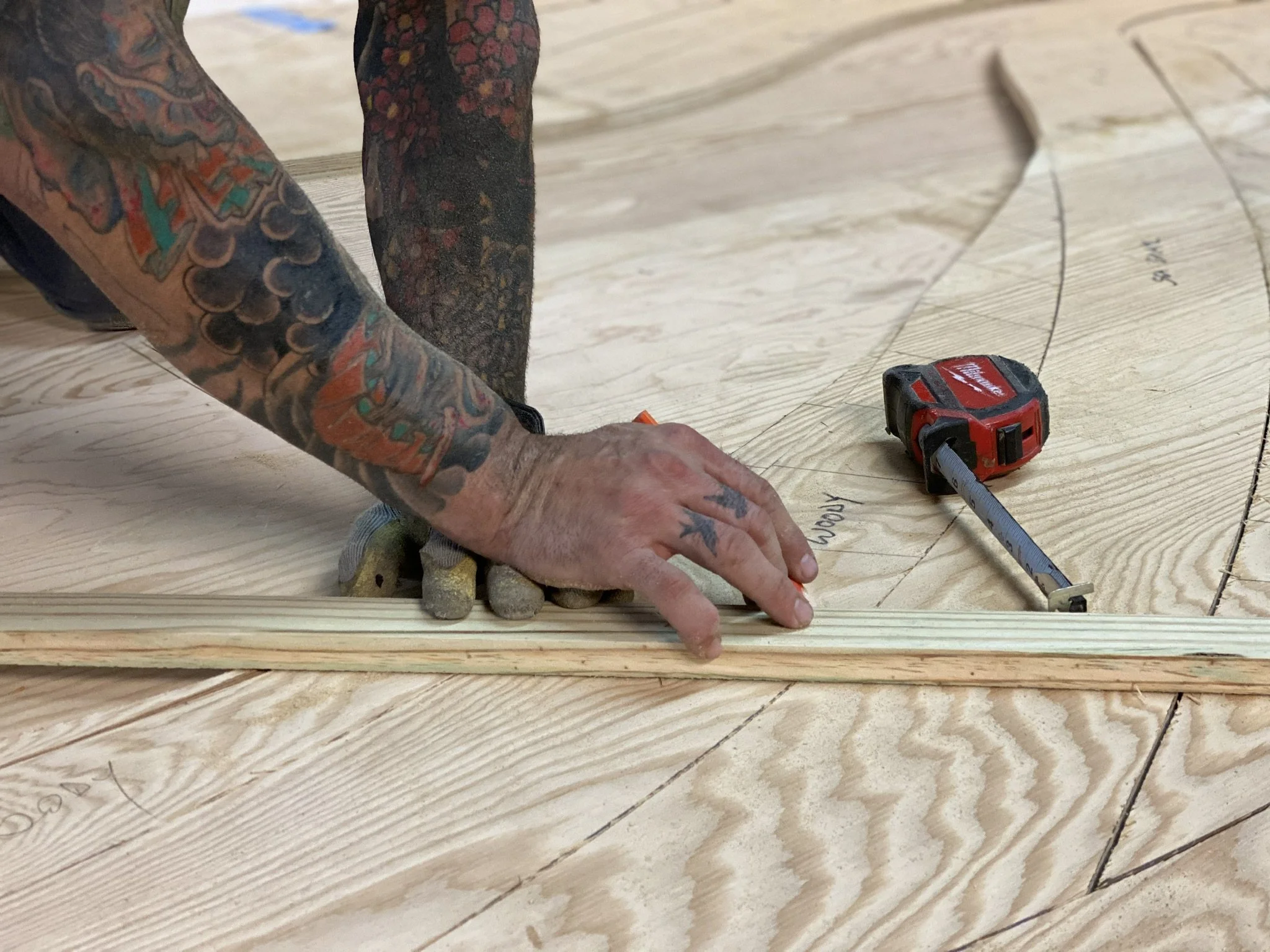 A tattoed mans hands drawing the pattern for a custom wood wall art piece for the Virgin Voyages Resort in Bimini, Bahamas.