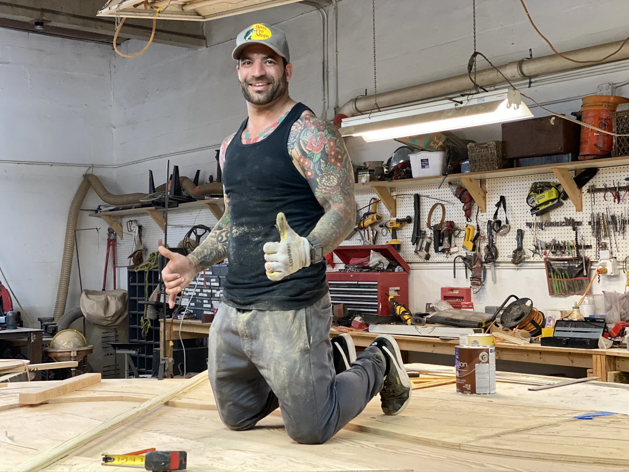 A tattooed man sits on an art piece that is being hand crafted.
