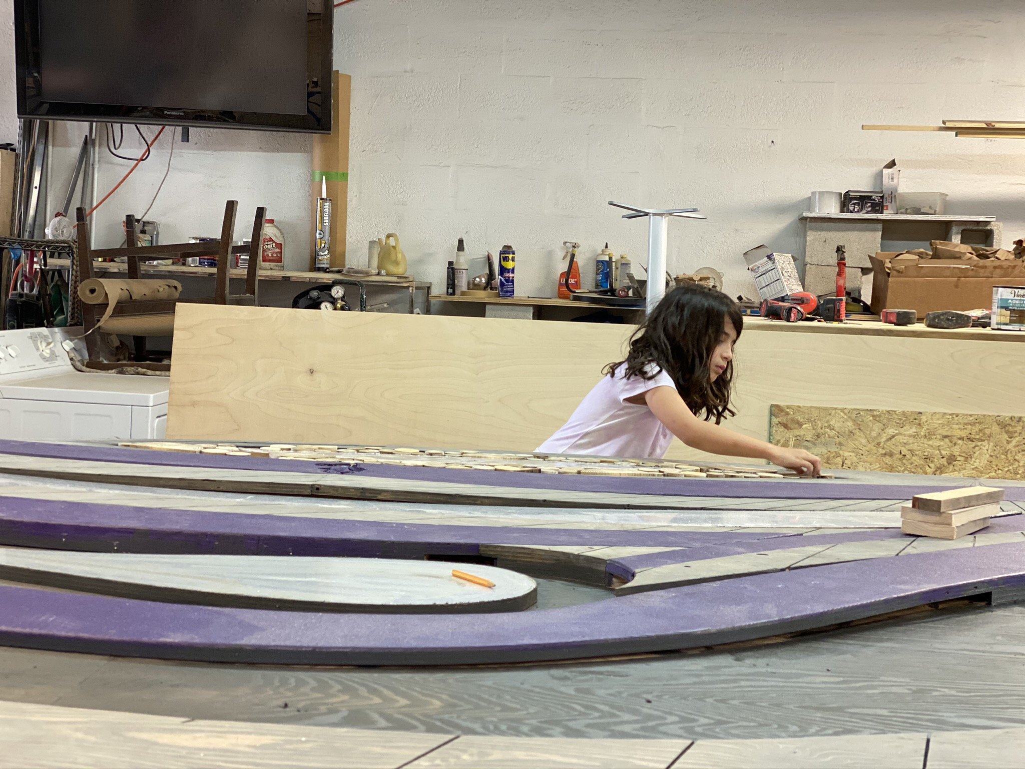 A young girl hand crafts wooden wall art for Virgin Voyages art commission in a carpentry workshop.