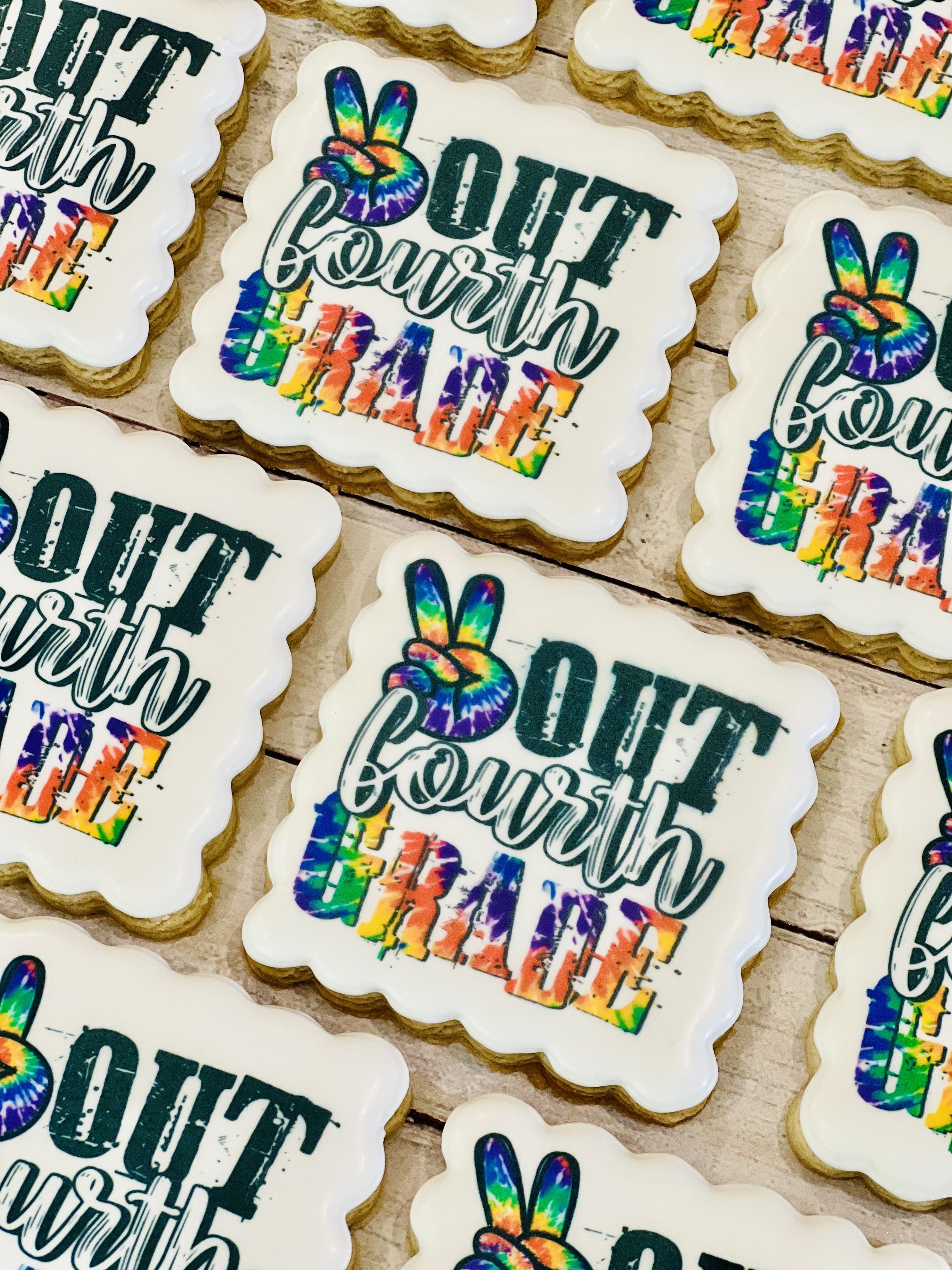Decorated cookies with the phrase "Out Fourth Grade" and a peace sign, featuring colorful rainbow designs on white backgrounds.