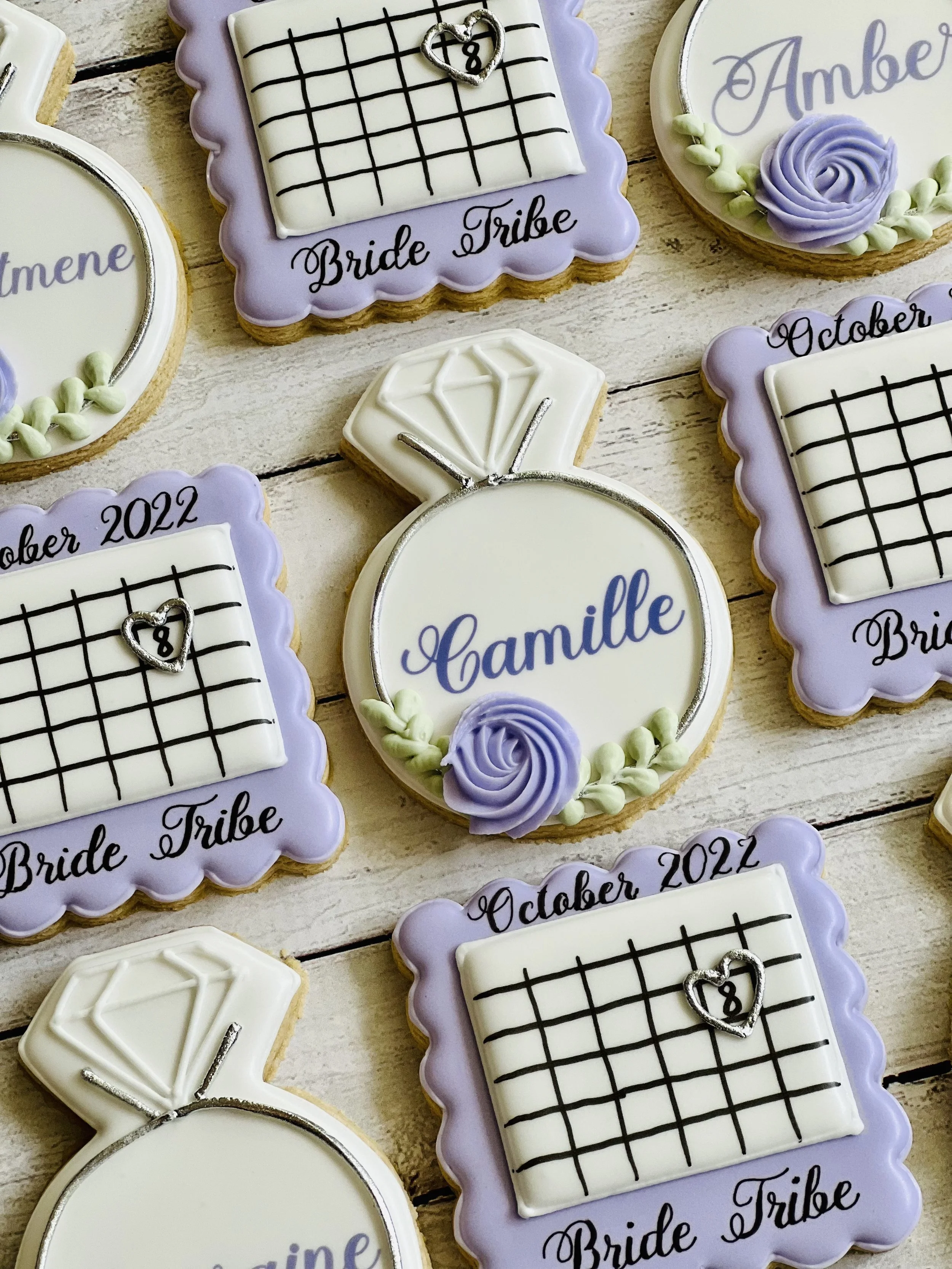Decorative cookies shaped like rings and squares with purple icing, featuring names, calendar designs, and "Bride Tribe" text.