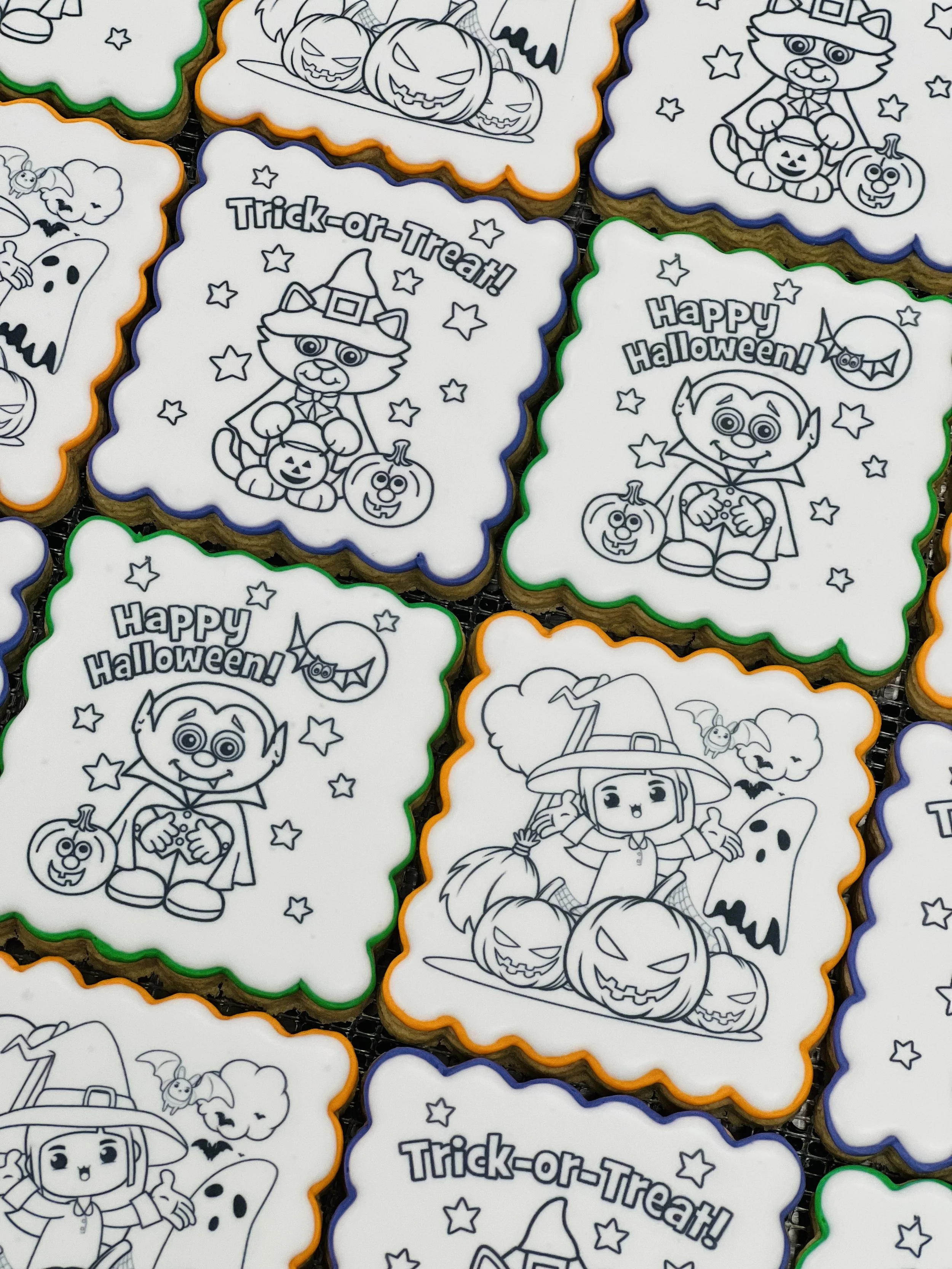 Halloween-themed cookies with outline drawings of a cat dressed as a witch, a vampire, and a witch surrounded by pumpkins, ghosts, and bats. The cookies have messages like "Trick-or-Treat!" and "Happy Halloween!" with colorful icing borders.