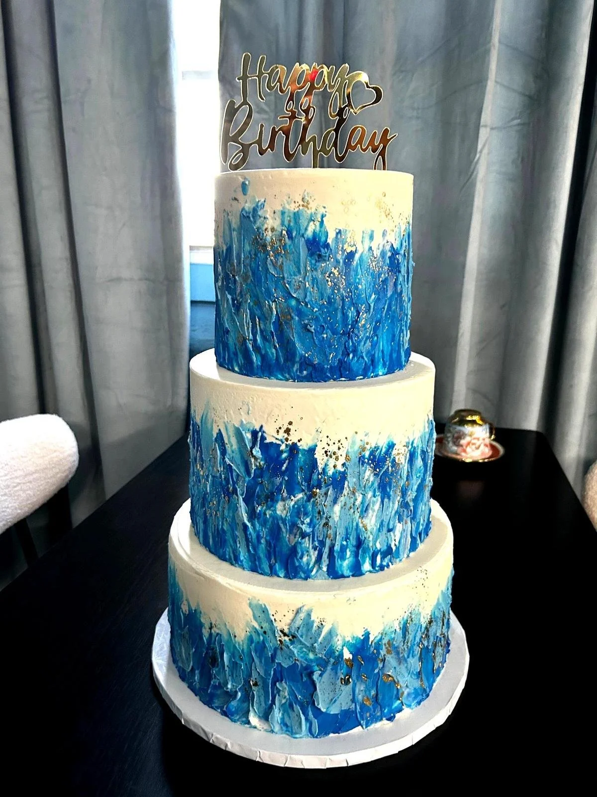 Three-tiered birthday cake with blue and white abstract design and 'Happy Birthday' topper.