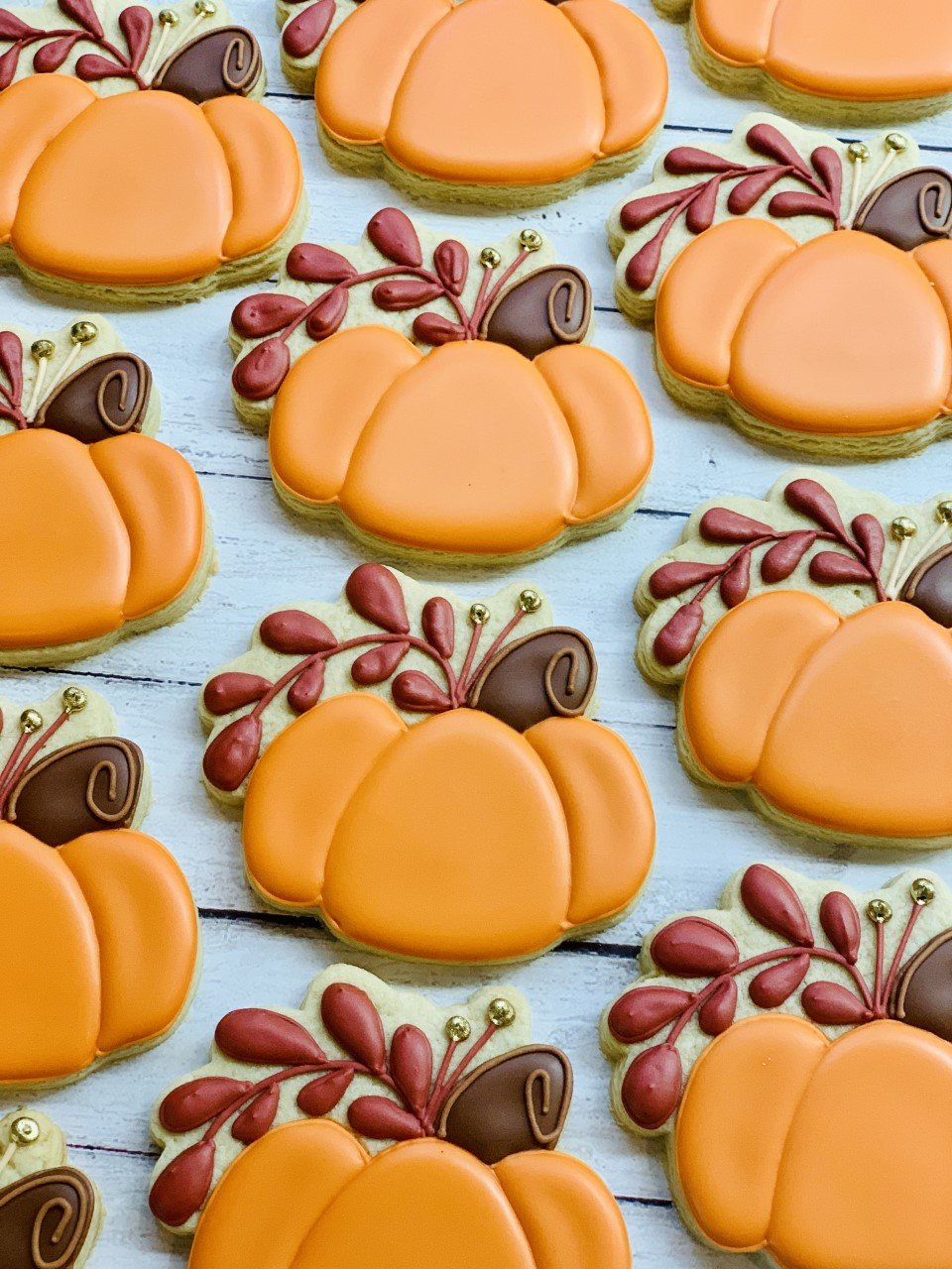 Decorated pumpkin-shaped cookies with orange icing and red and brown accents on a white wooden background.