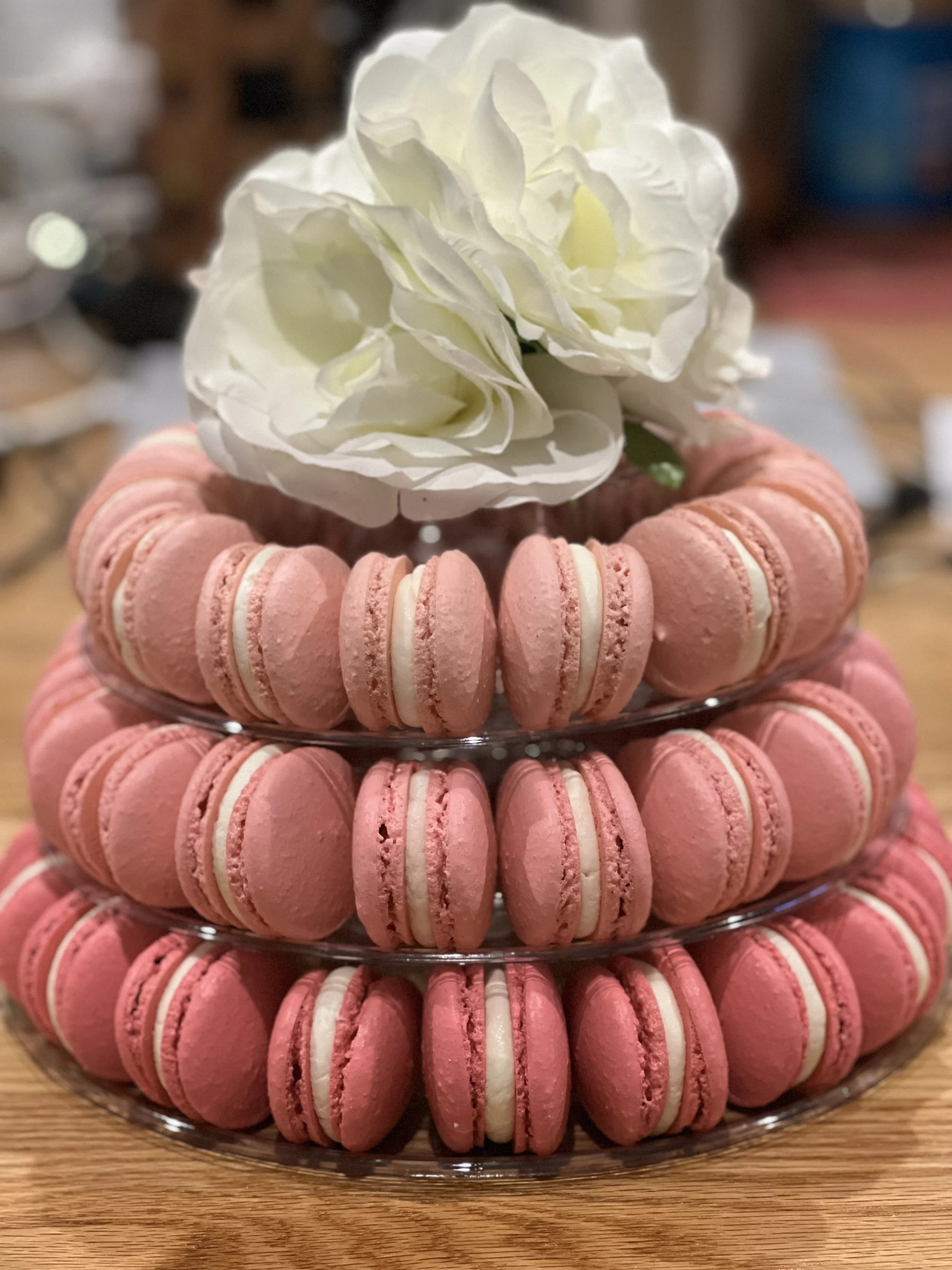 A three-tier stand with pink macarons and white flowers on top.