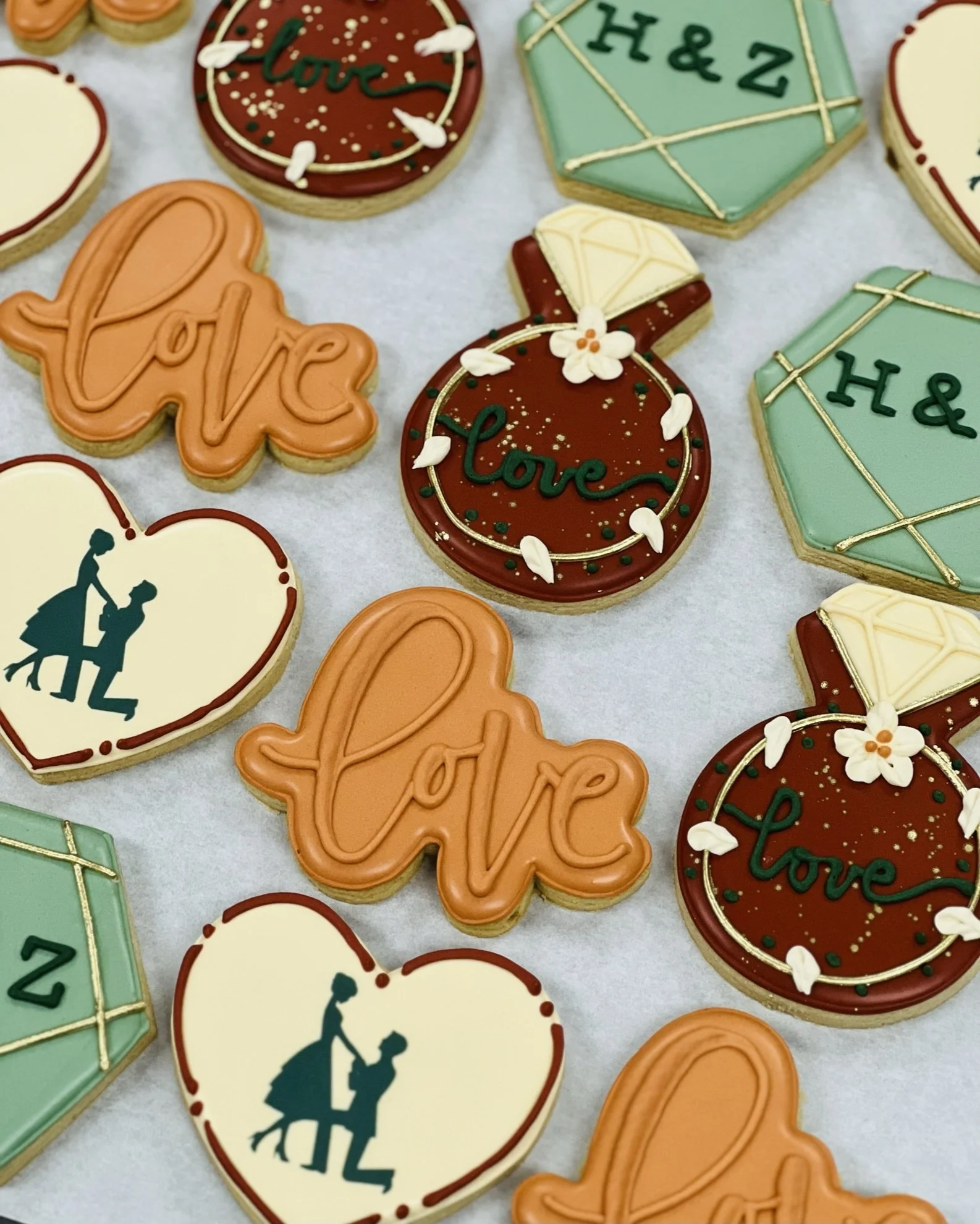 Decorated cookies with engagement theme, featuring shapes like hearts, rings, and hexagons, with words 'love' and initials 'H & Z' in various colors.