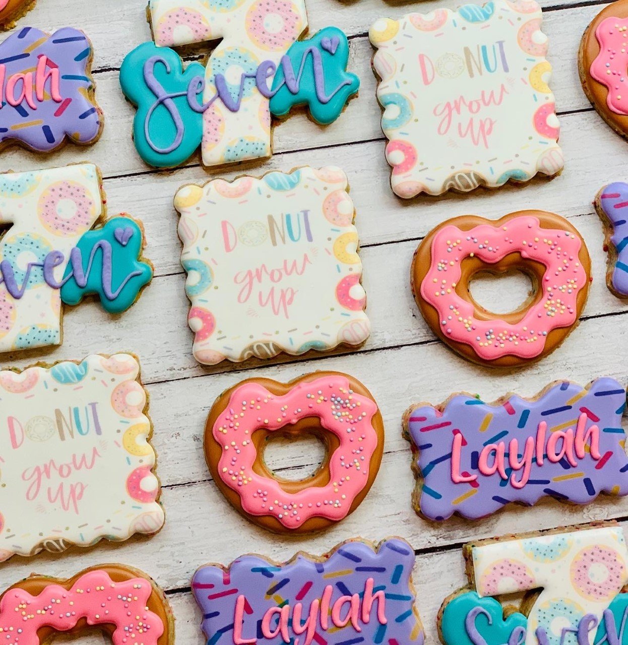Colorful decorated cookies with frosting, featuring phrases like "Donut grow up" and names like "Laylah." The designs include donuts and the number seven.