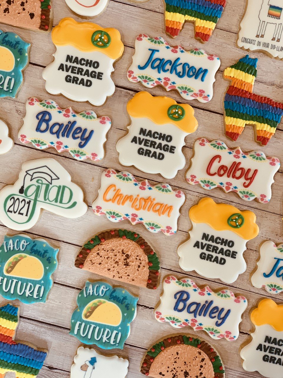 Decorative graduation-themed cookies with names and puns, featuring designs like tacos, colorful piñatas, and phrases such as "Nacho Average Grad" and "Taco 'bout a future!"