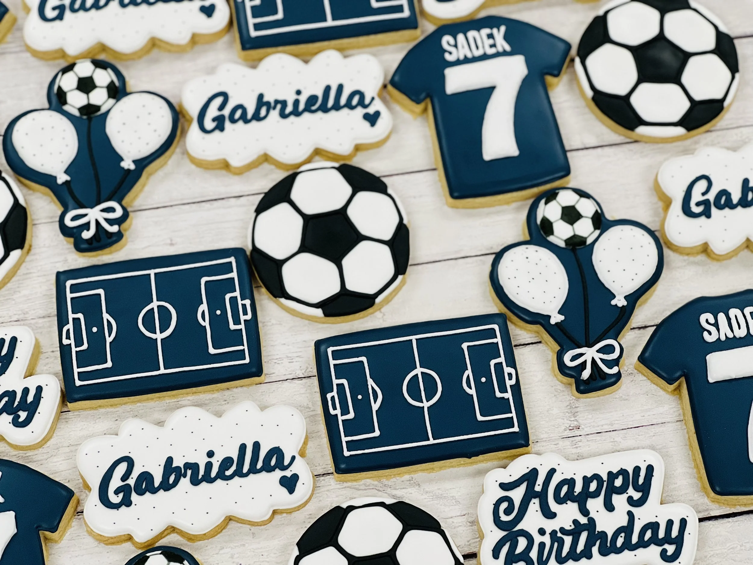 Assorted soccer-themed cookies including jerseys, soccer balls, and fields, with some personalized and "Happy Birthday" inscriptions.