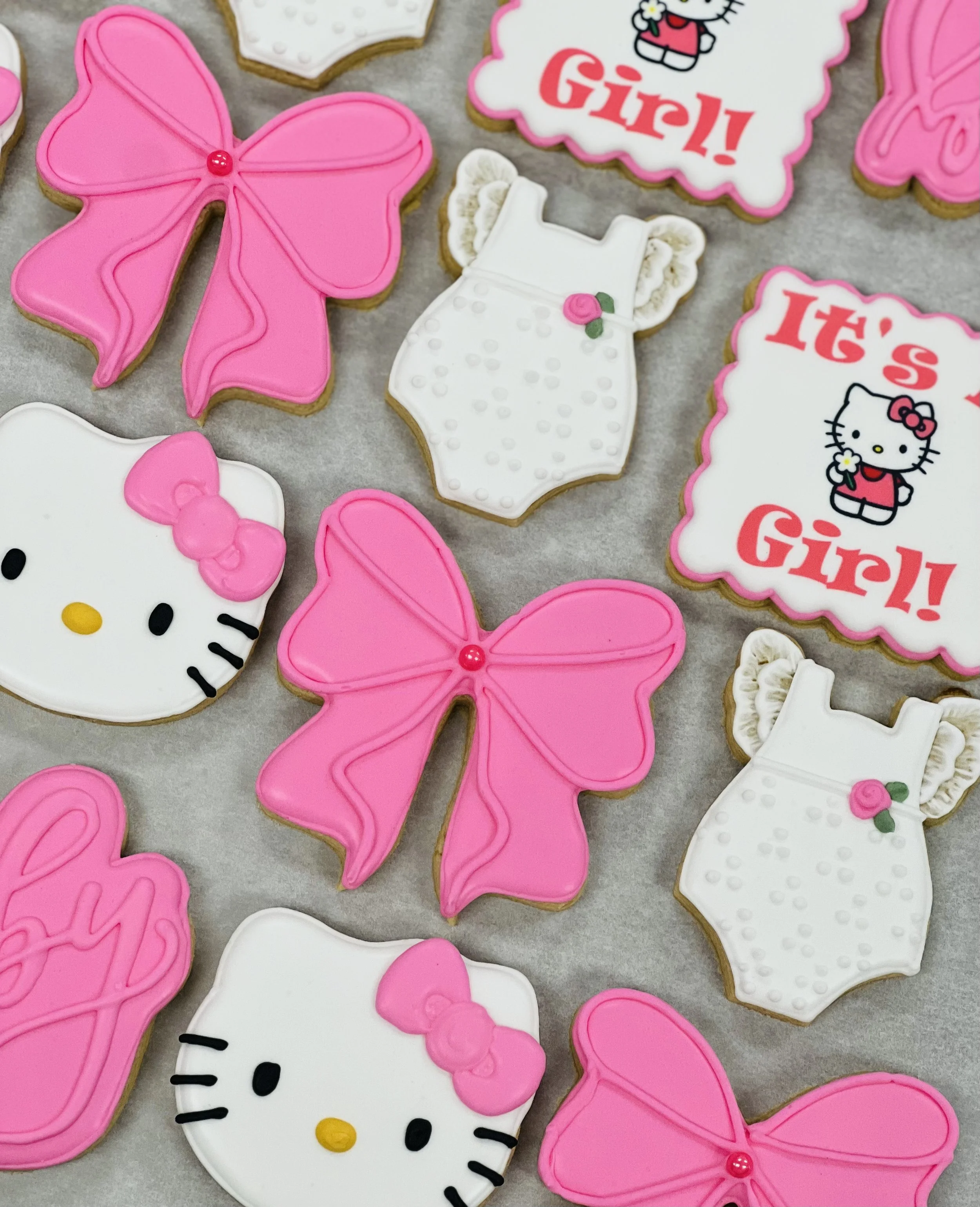 Assorted baby shower cookies with Hello Kitty, pink bows, and baby-themed designs.