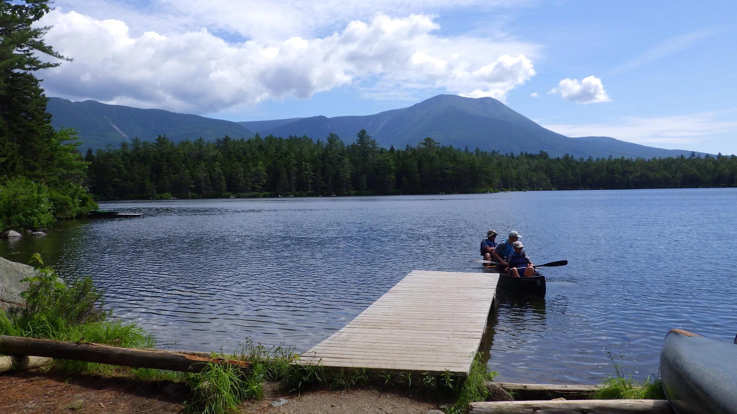 two people in a canoe at the end of a dock overlooking Katahdin in the distance