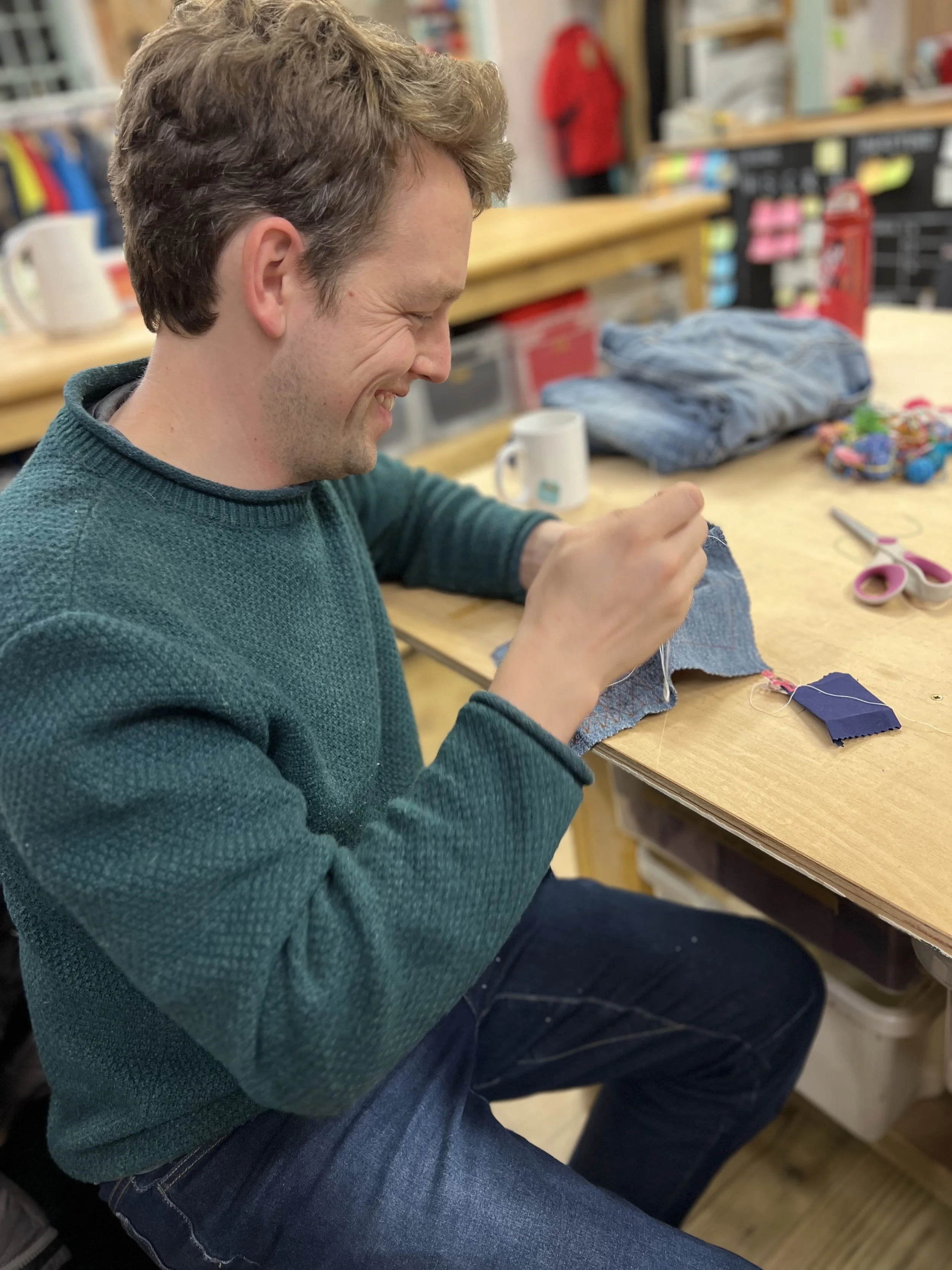 a man smiles contentedly while sewing sashiko style stitching on a swatch of denim
