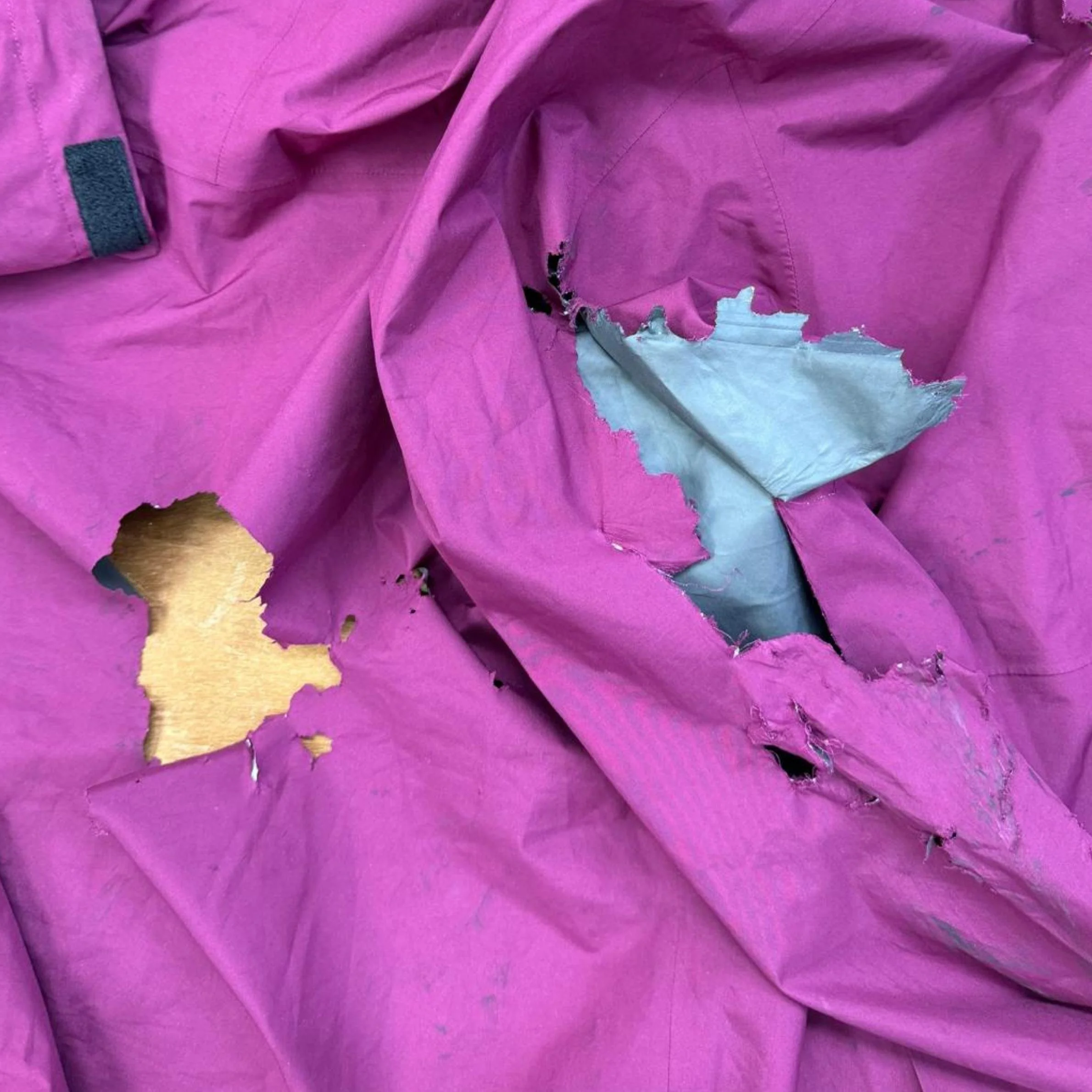 Pink Gore-tex jacket on wood cutting table with gaping holes
