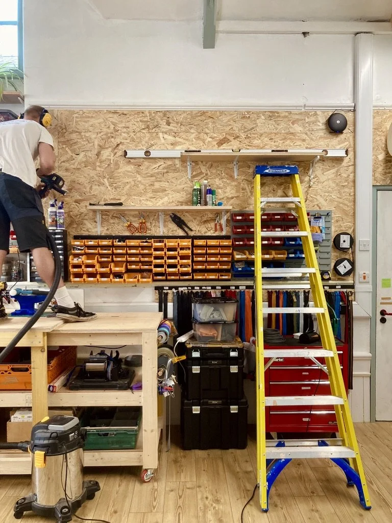 a man stands on a table, using a shop vacuum to put the finishing touches on newly built shelves