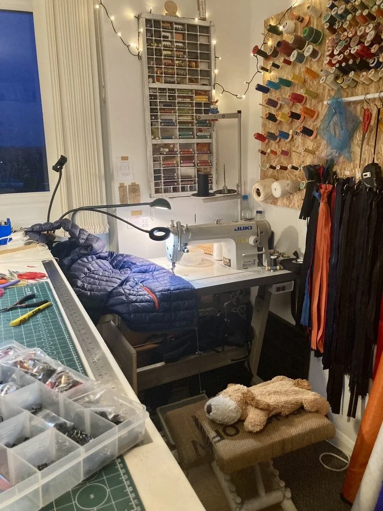a home sewing workshop with cutting table, industrial machine, thread board, and hot water bottle on the chair
