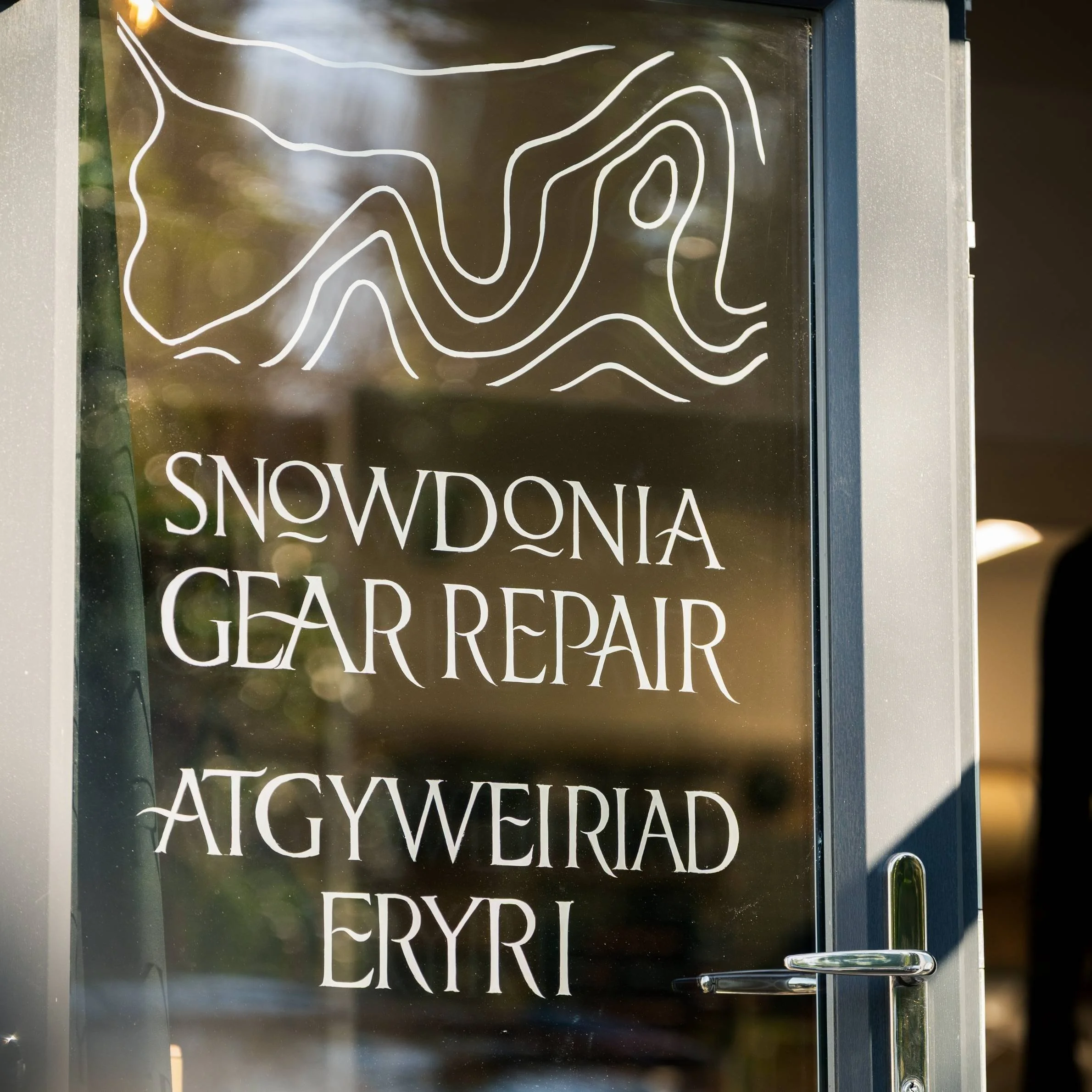 A photo of the front door of Snowdonia Gear Repair, with green reflected in the glass.