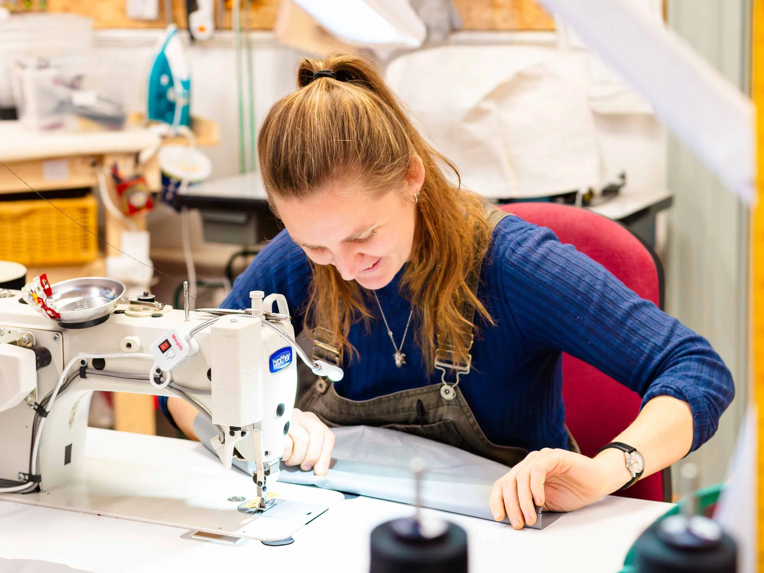 woman folding fabric at sewing machine in brightly lit workshop