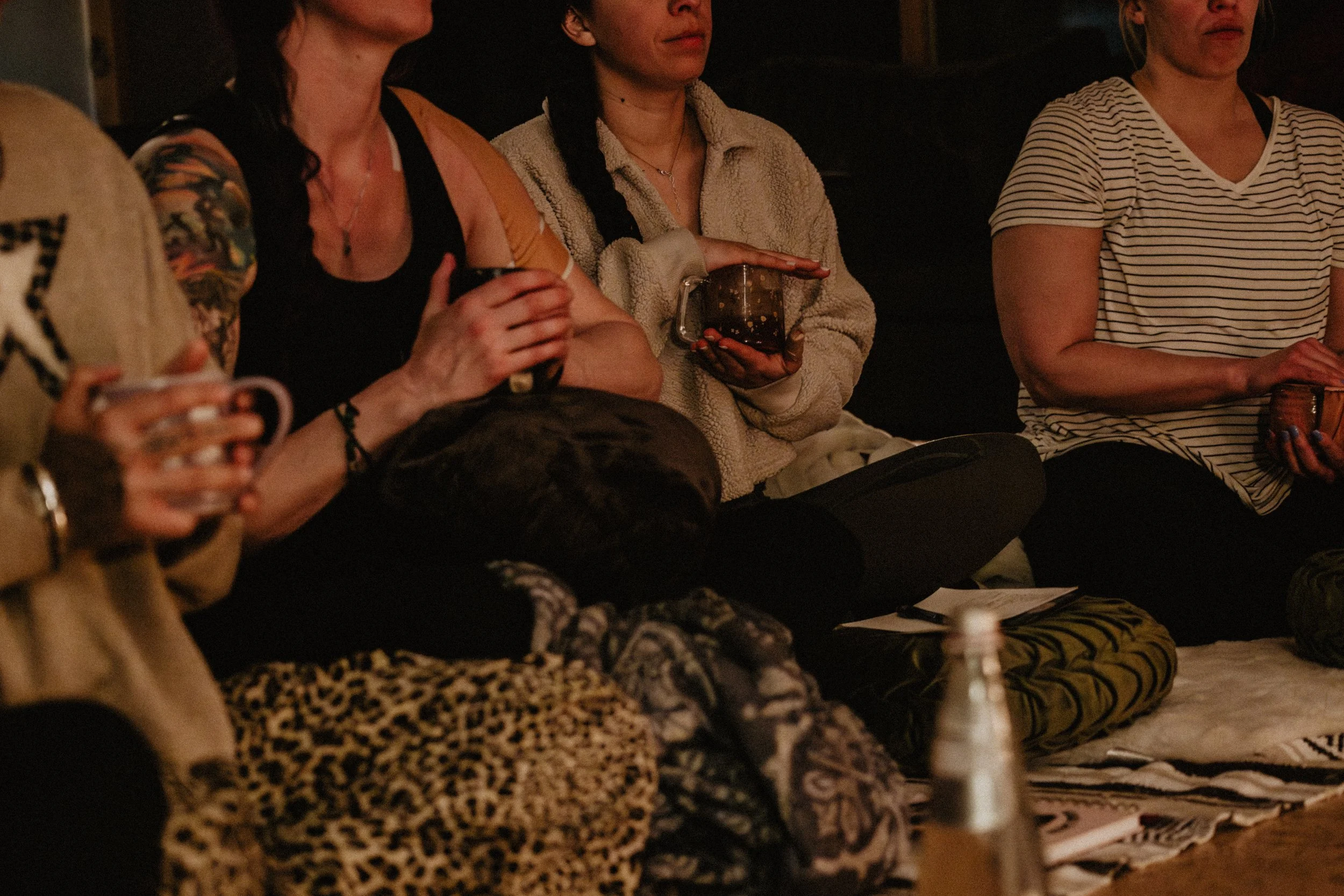 People sitting on the floor with notebooks and drinks, possibly in a casual meeting or discussion.