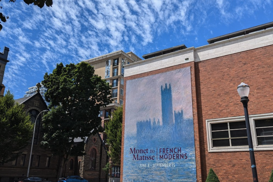 Large outdoor advertisement for an art exhibition titled "From Monet to Matisse: French Moderns," running from June 8 to September 15, on a brick building with a blue sky in the background.