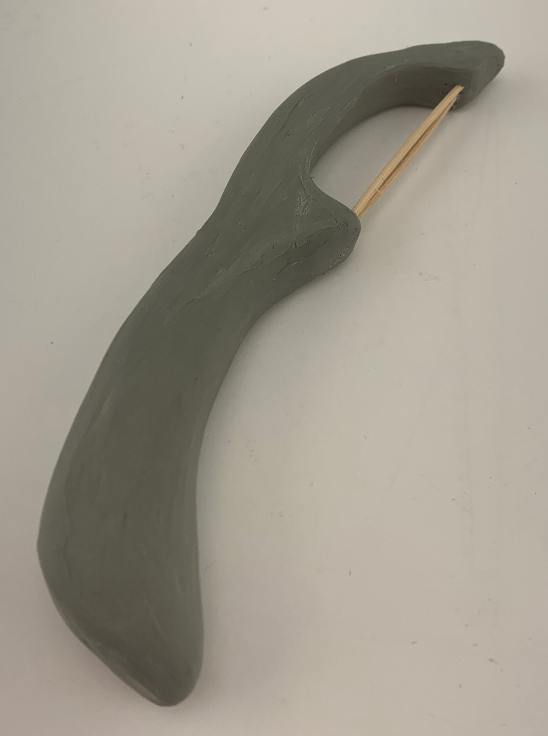 Handmade clay figurine resembling a boomerang with a small stick.