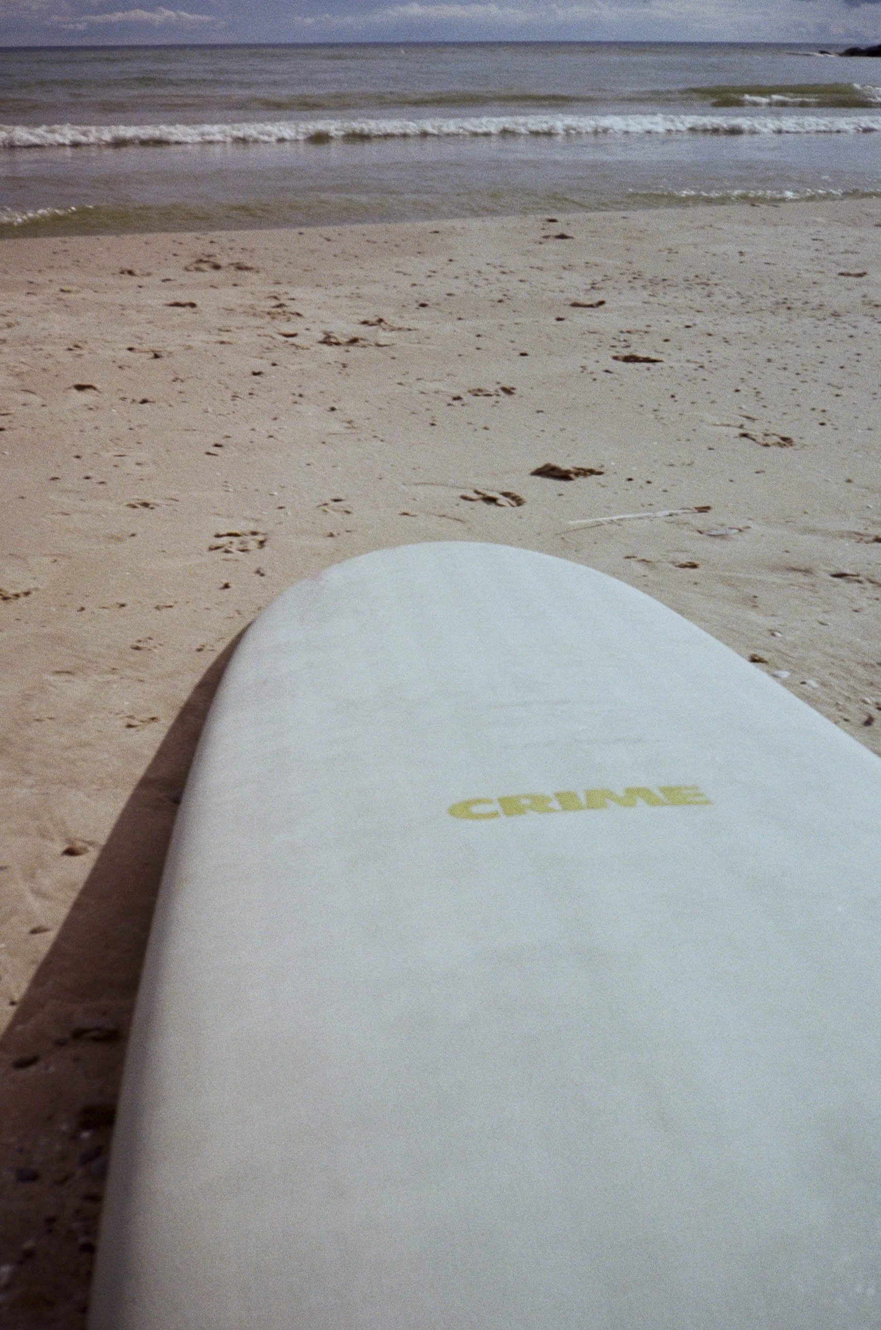 A surfboard lying on a sandy beach facing the ocean with gentle waves.