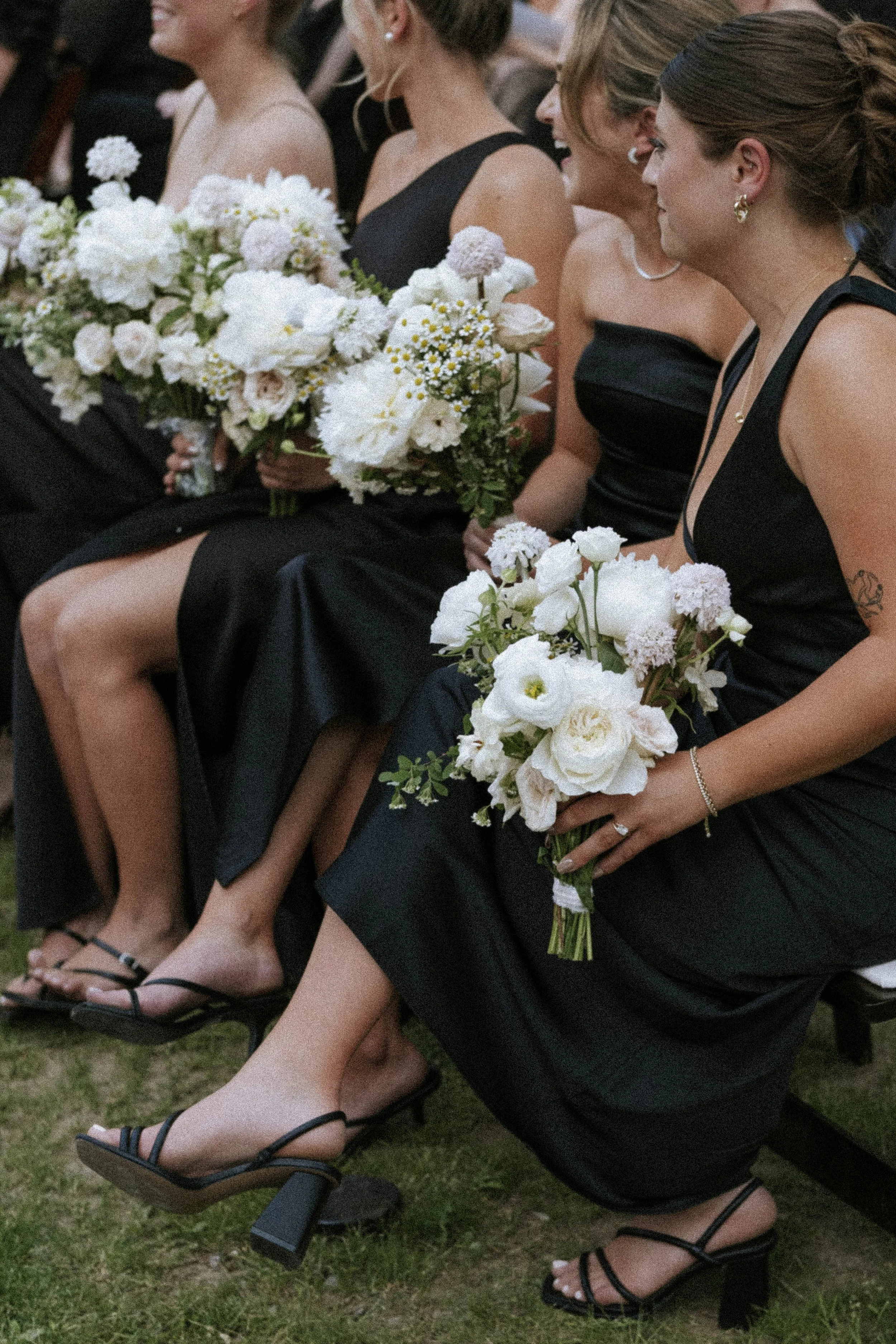 Women in black dresses sitting and holding bouquets of white flowers at an event.