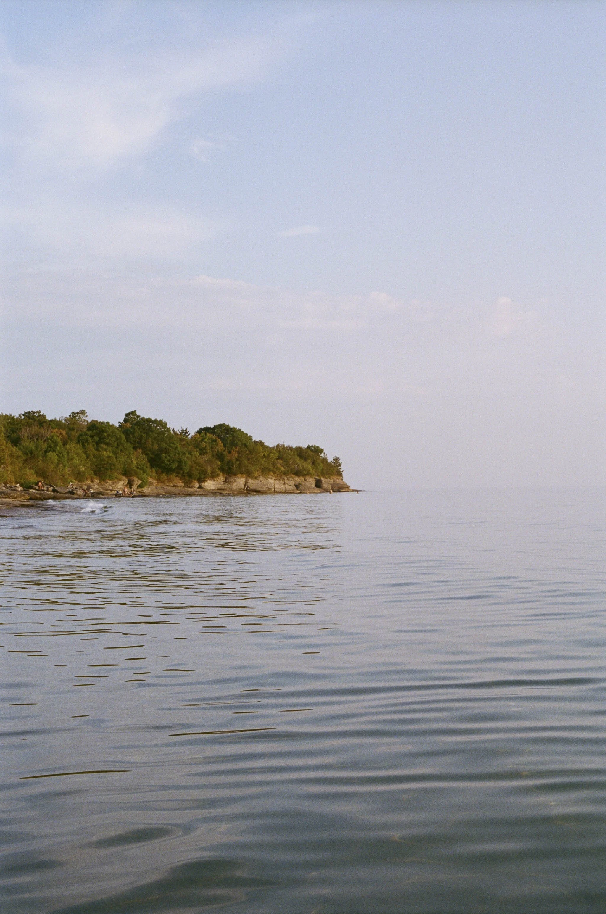 Calm lake water with a rocky, tree-lined shoreline on the horizon and a partly cloudy sky.