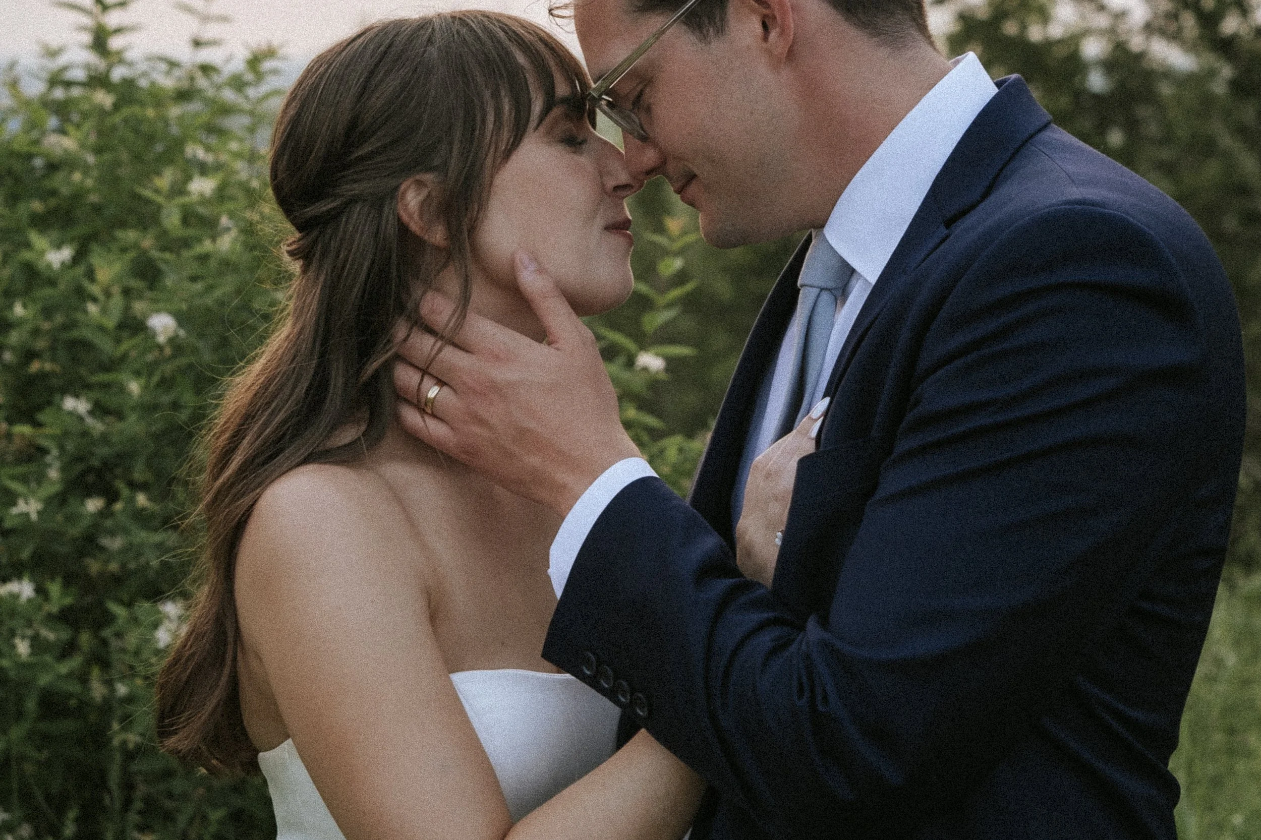 A romantic moment between a man and woman outdoors, with their foreheads touching and eyes closed, the man holding the woman's face gently.