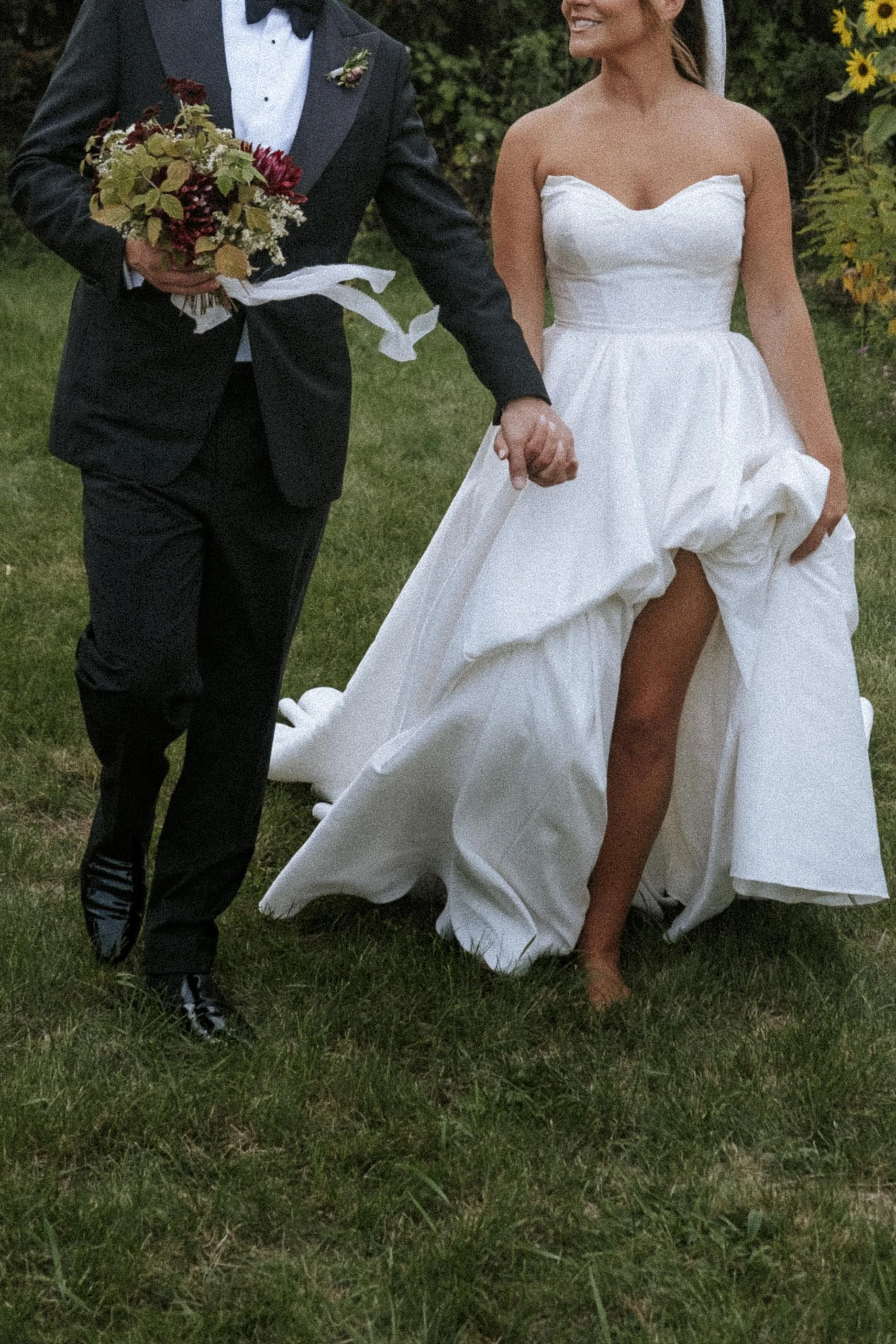 A bride and groom holding hands during a wedding, with the bride lifting her wedding dress to show her leg.