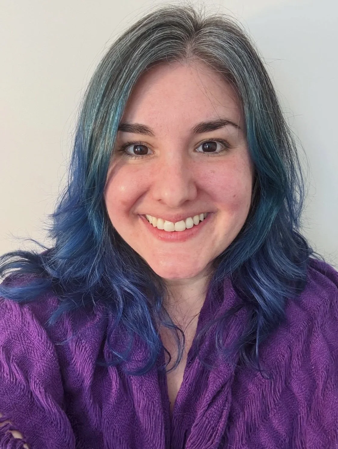 Dr. Marussia Role - a smiling White, non-binary person with gray, black, and blue hair. They are wearing a bright purple, woven scarf.