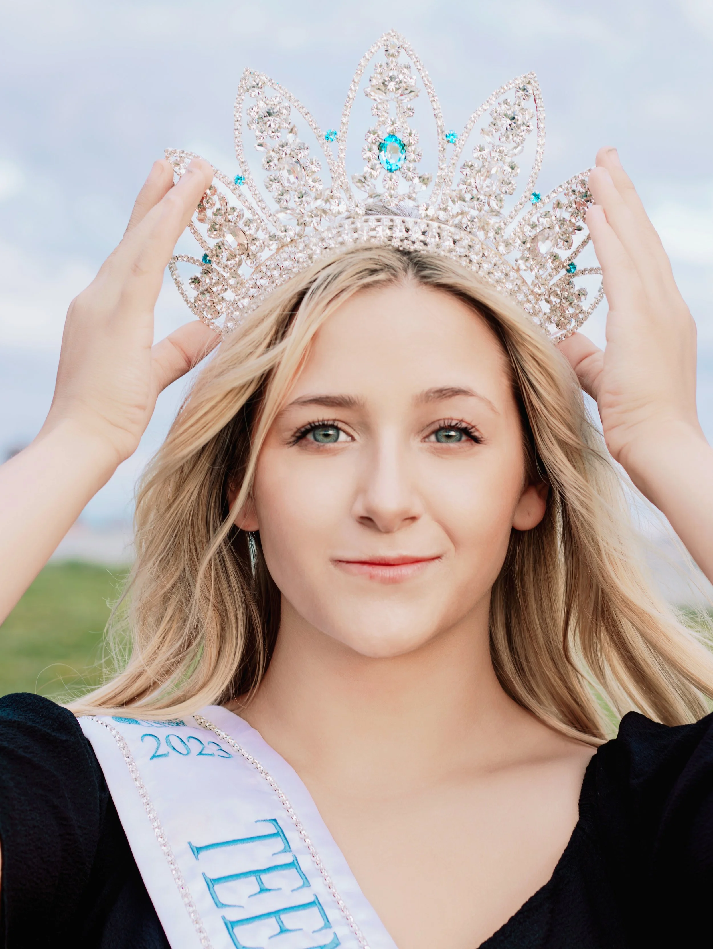 Young woman with blonde hair and blue eyes, wearing a crown and a sash that reads "2023 Miss Teen".