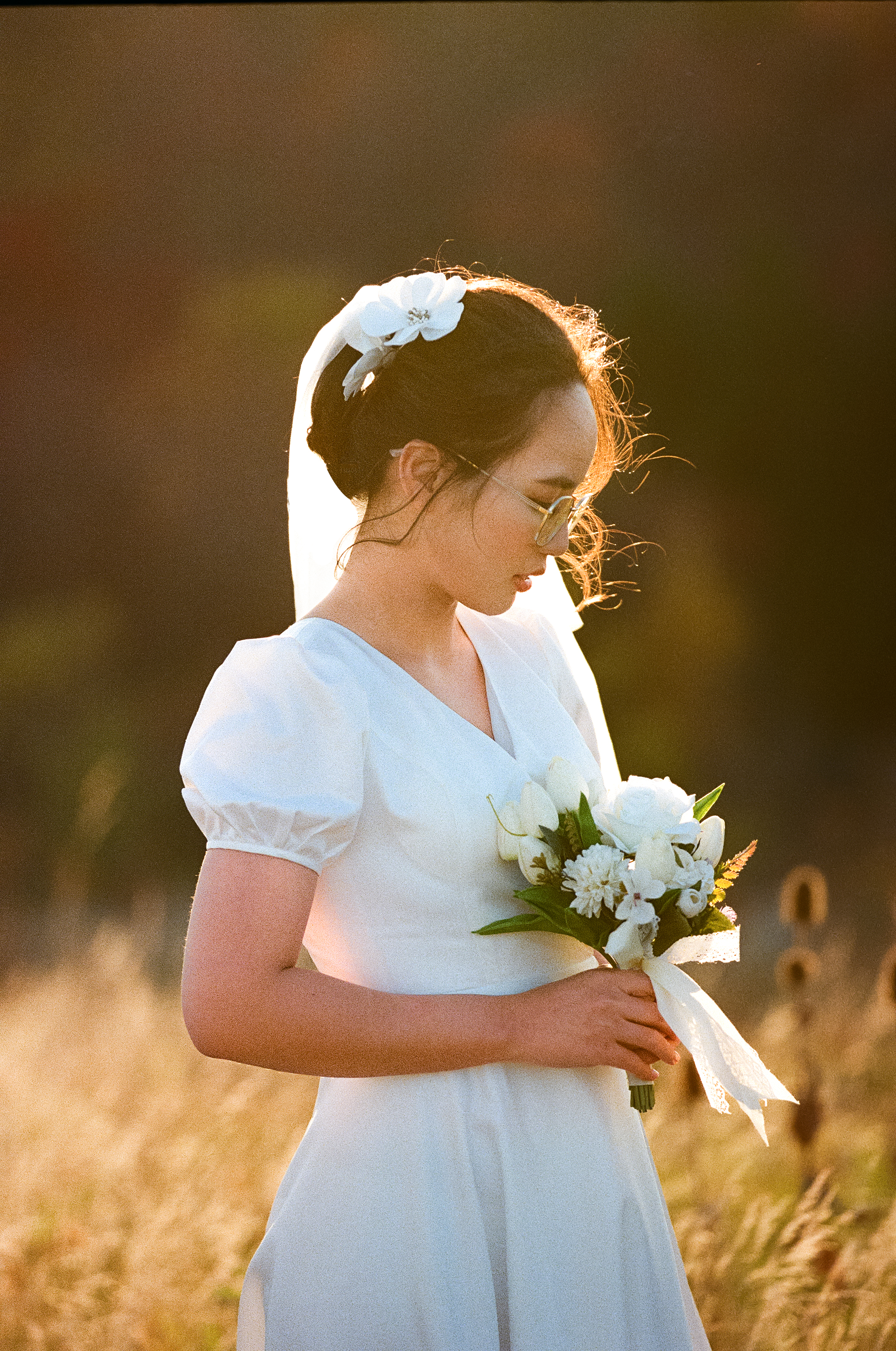 A woman in a white dress holding a bouquet of flowers, standing outdoors during sunset.