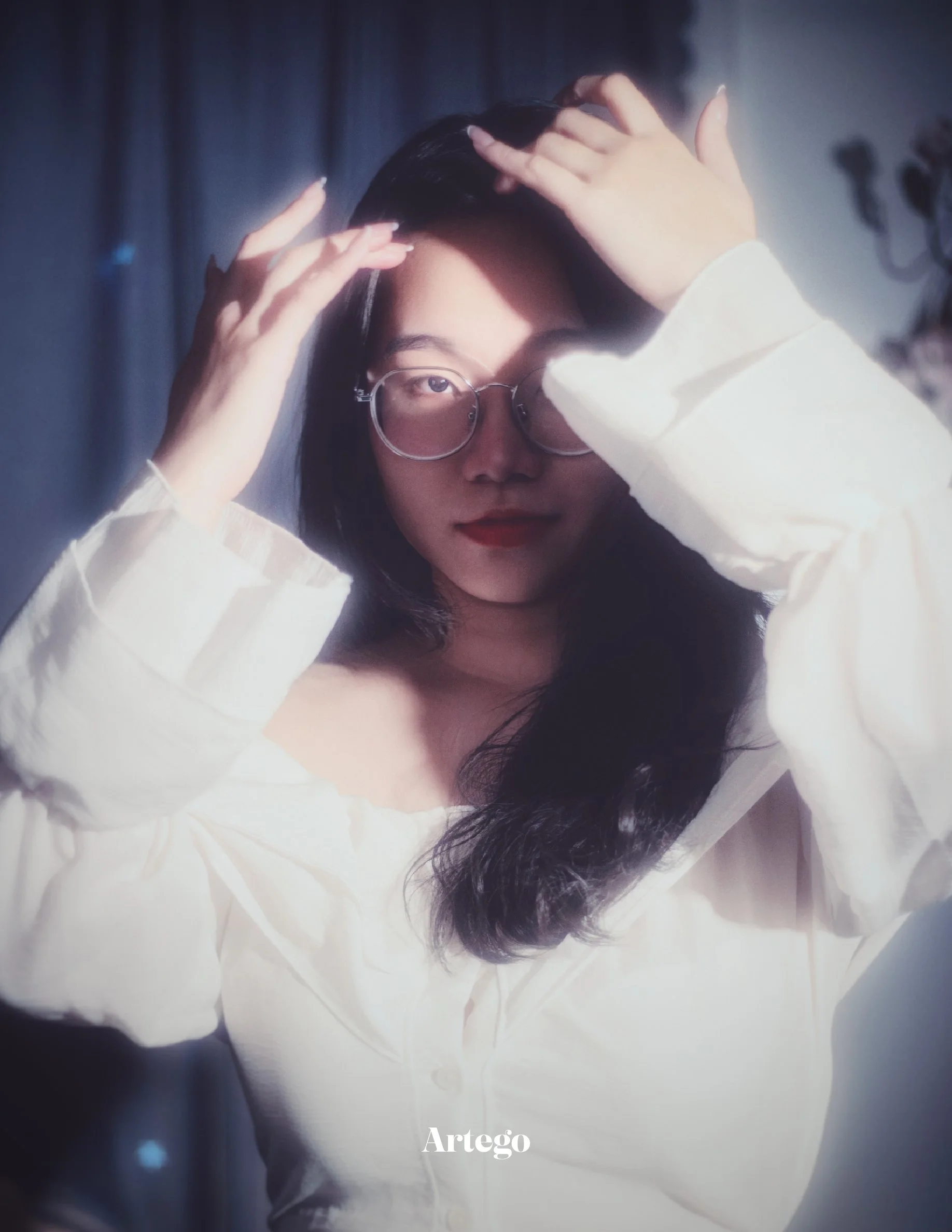 A woman with dark hair wearing glasses and a white shirt posing indoors.
