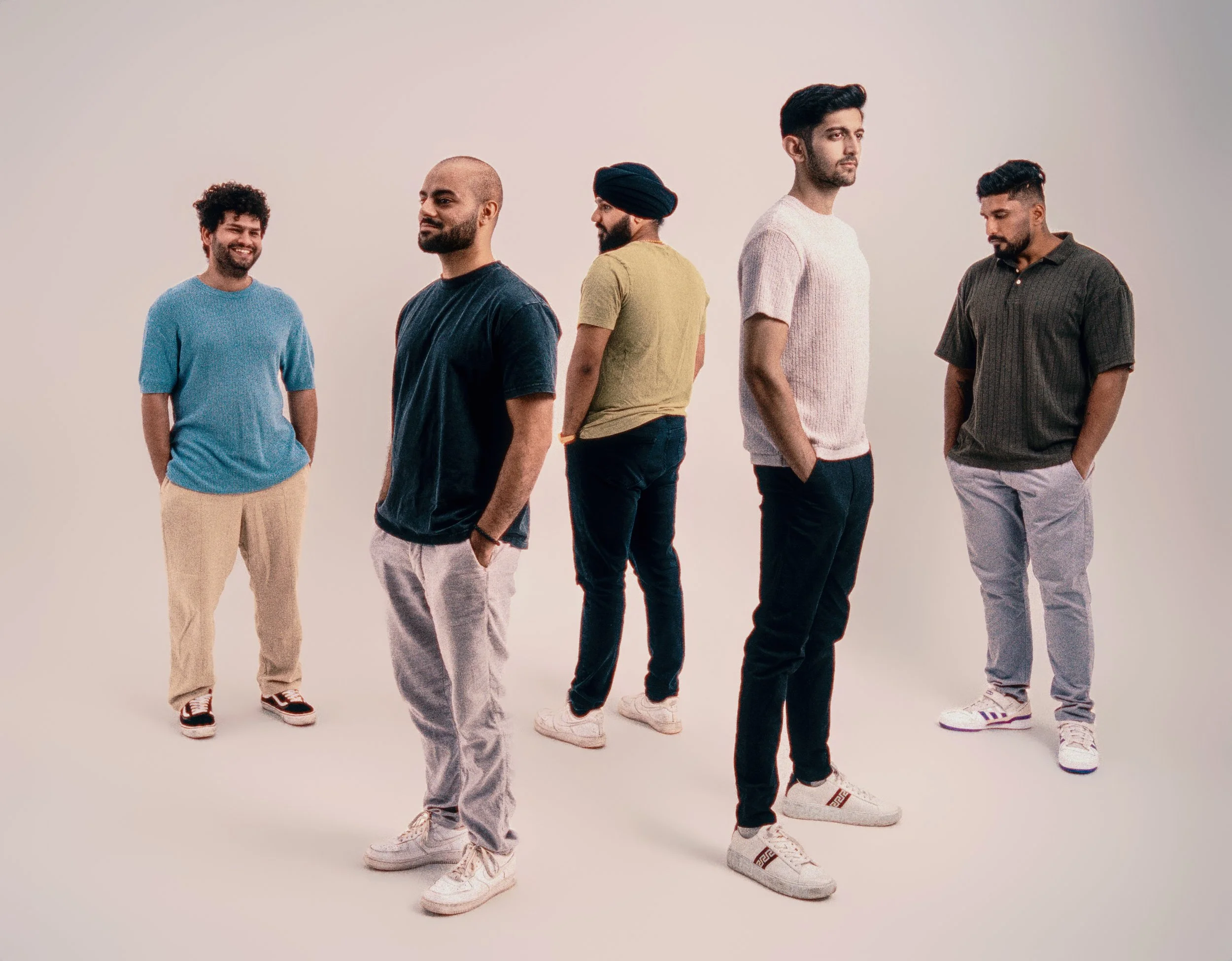 Six men standing in a formation on a plain white background, some facing forward, some turned to the side, wearing casual clothing.