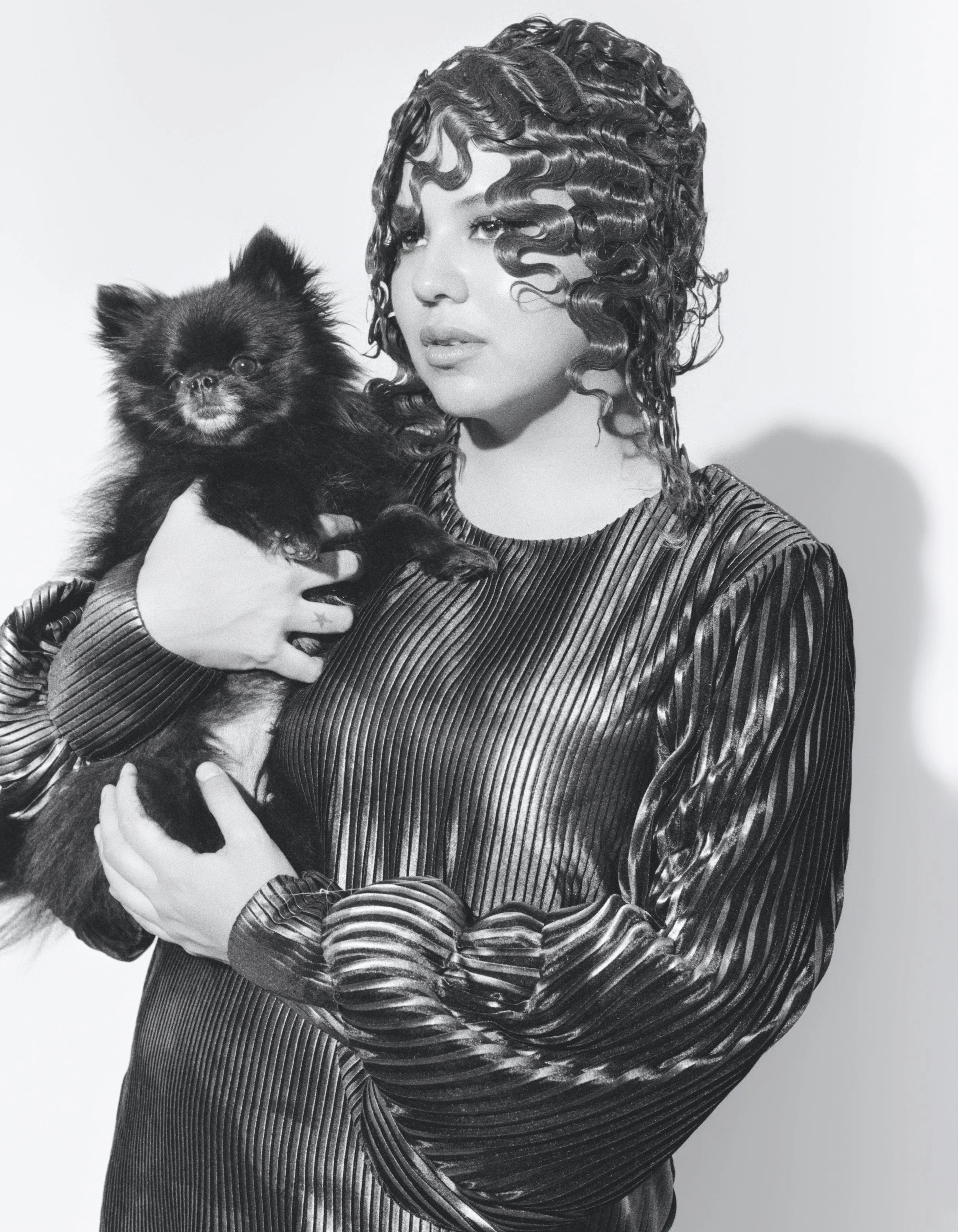A woman with curly hair holding a small black dog against a plain background.