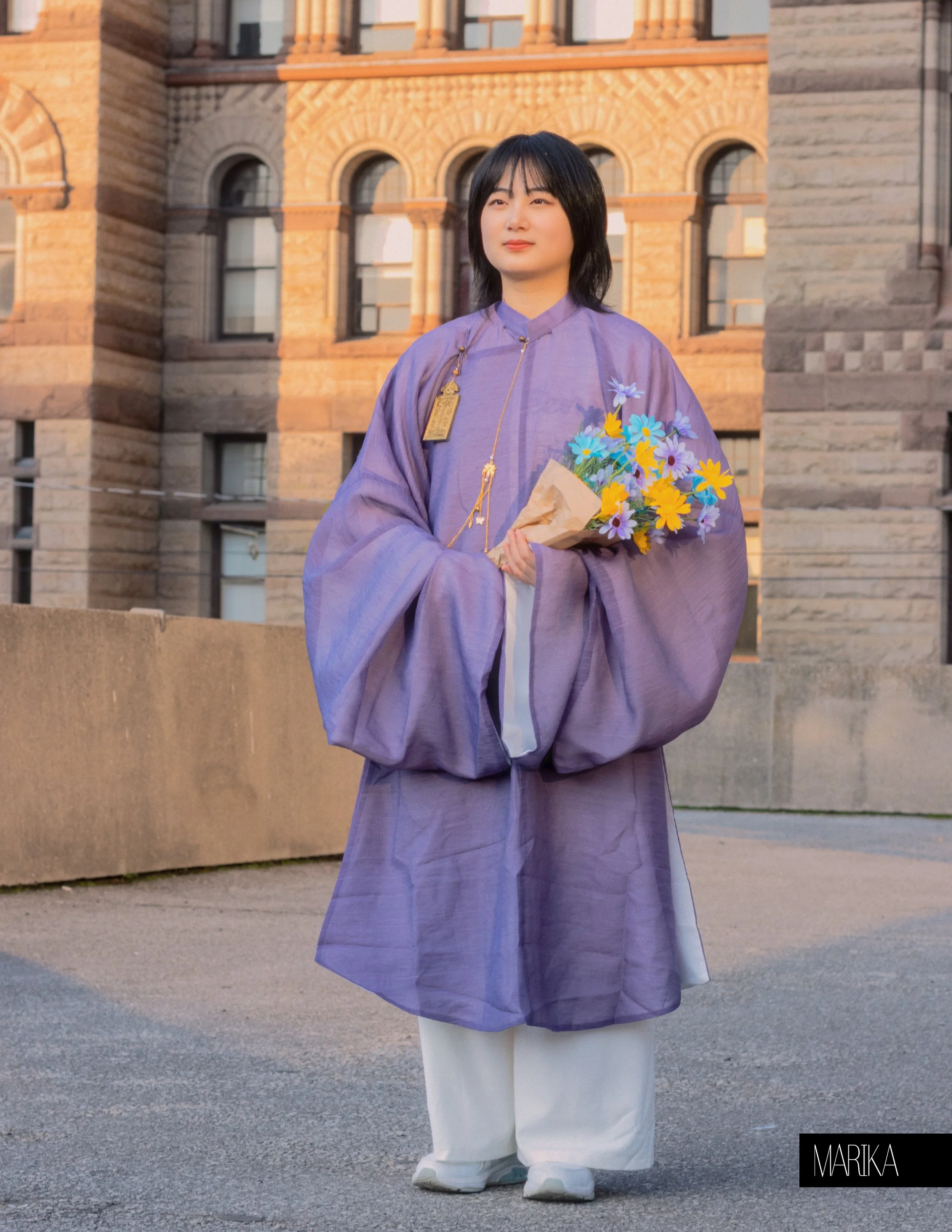 A woman in traditional Korean clothing holding a bouquet of flowers in front of a historical brick building.