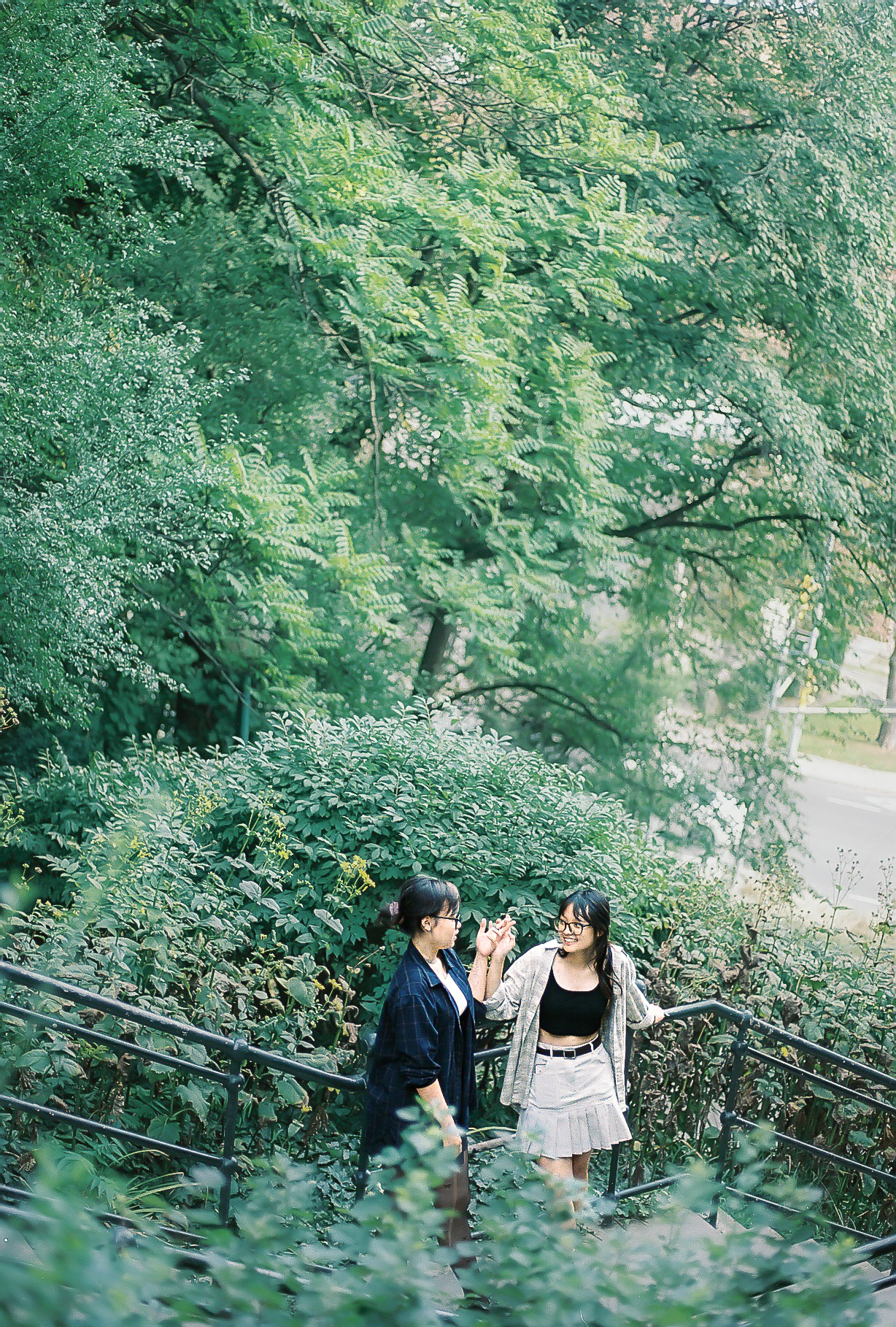 Two women talking on a staircase surrounded by green bushes and trees