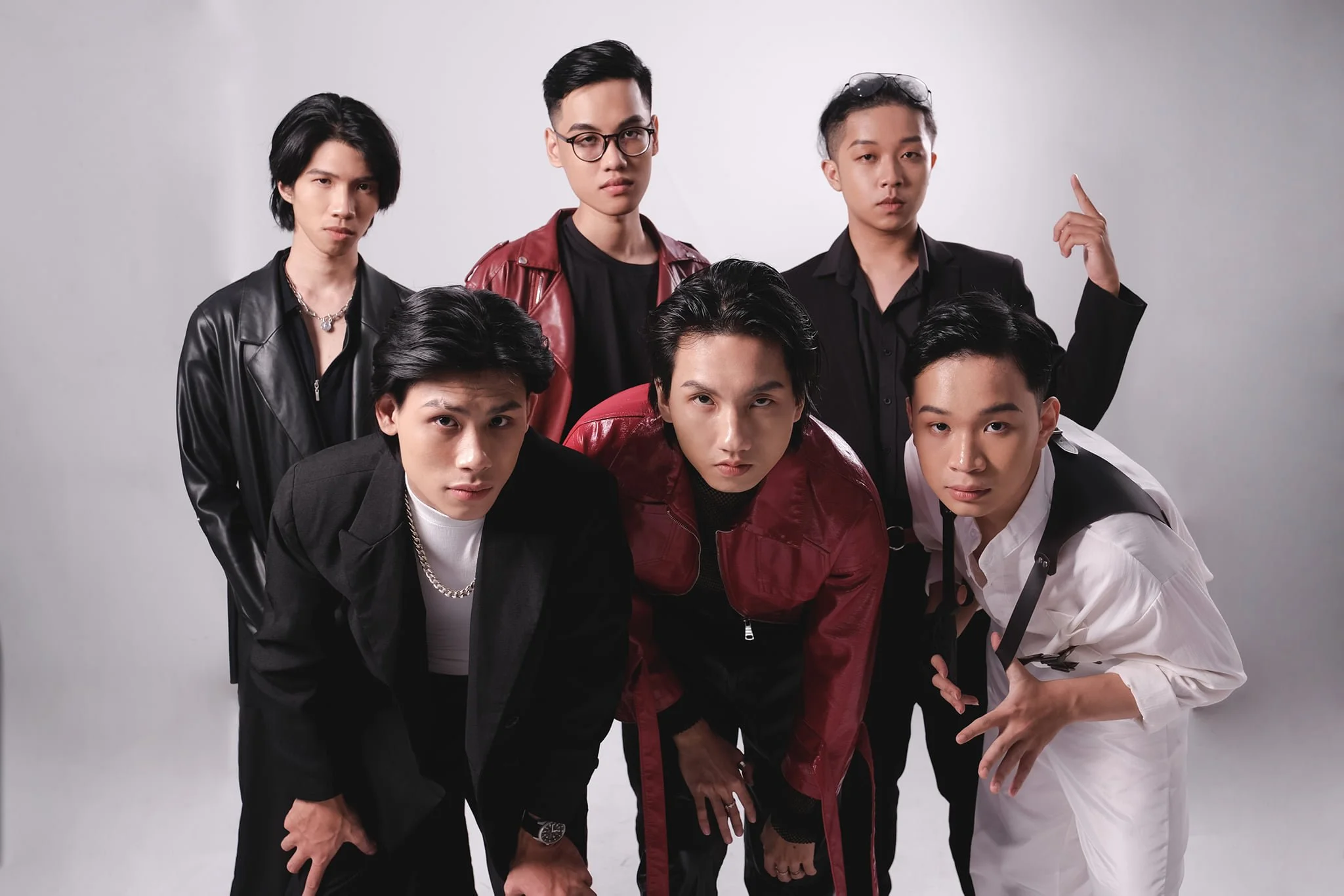 Group of seven young men posing together against a plain background, dressed in stylish urban clothing.