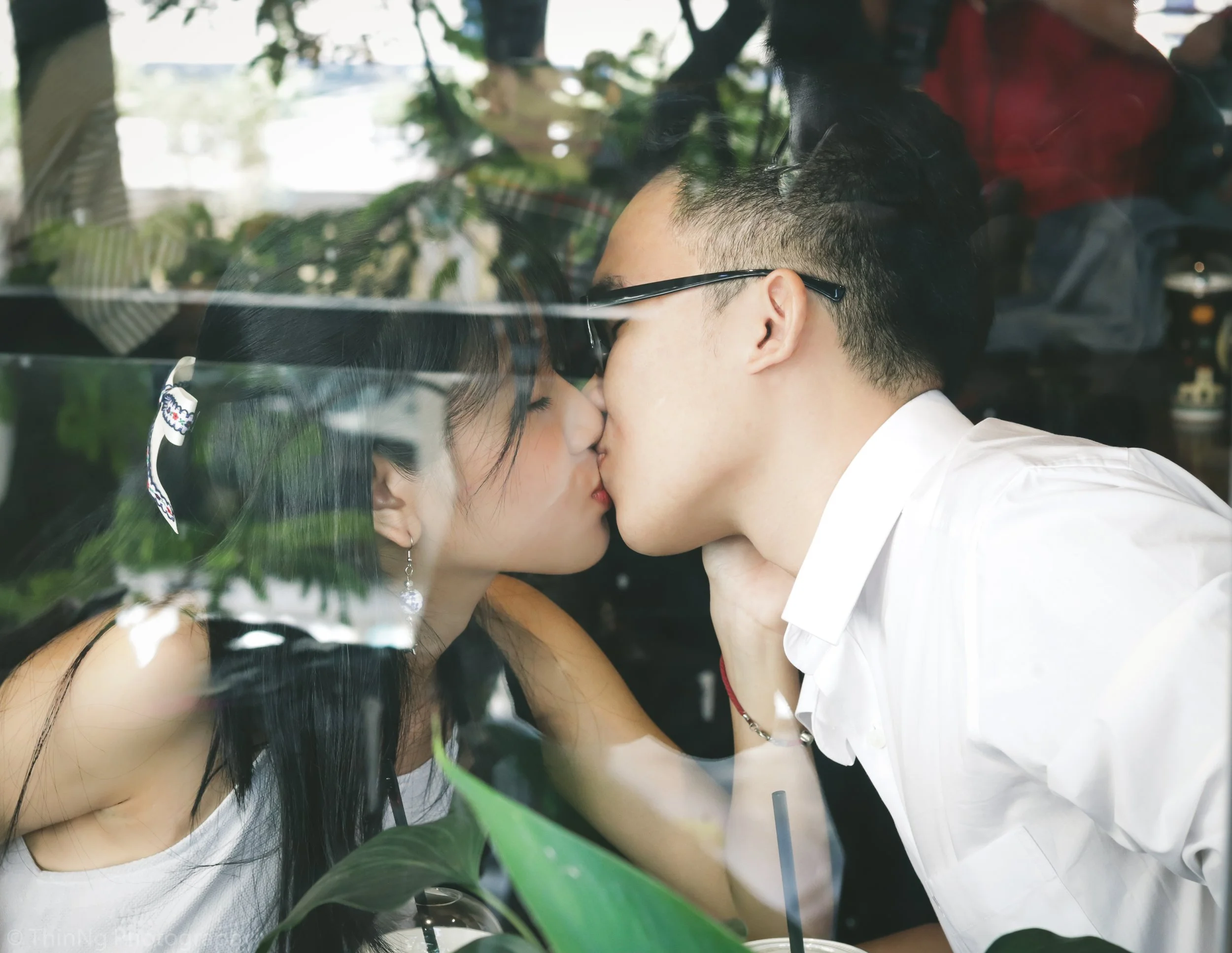 A couple sharing a kiss through a glass window at a cafe or restaurant.
