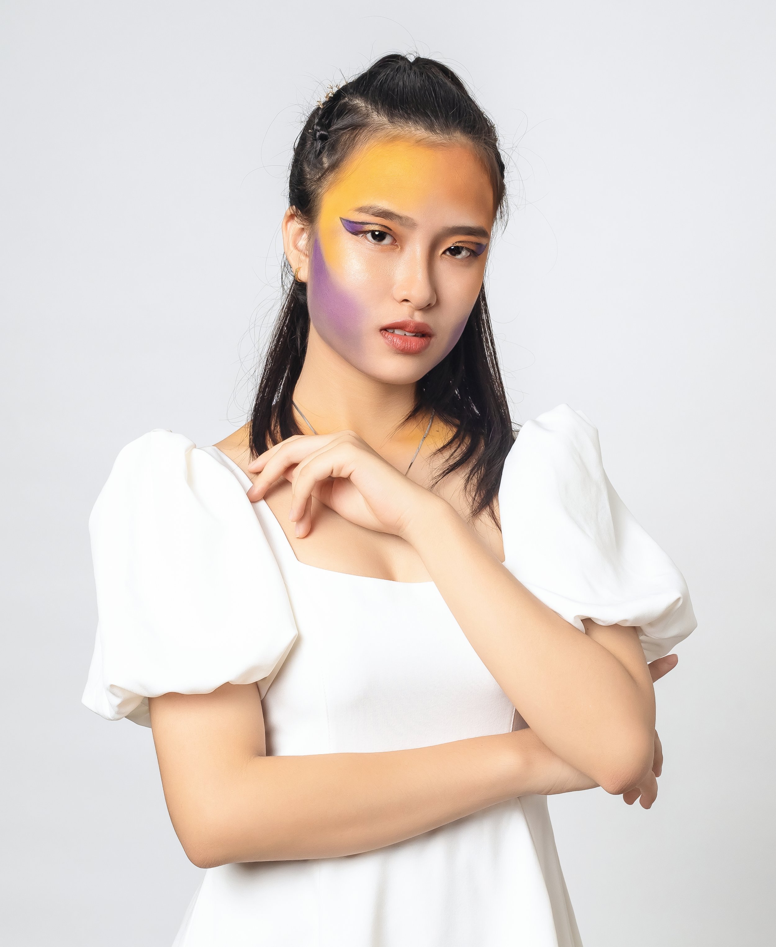 A young woman with colorful makeup, wearing a white dress with puffed sleeves, standing against a plain white background.
