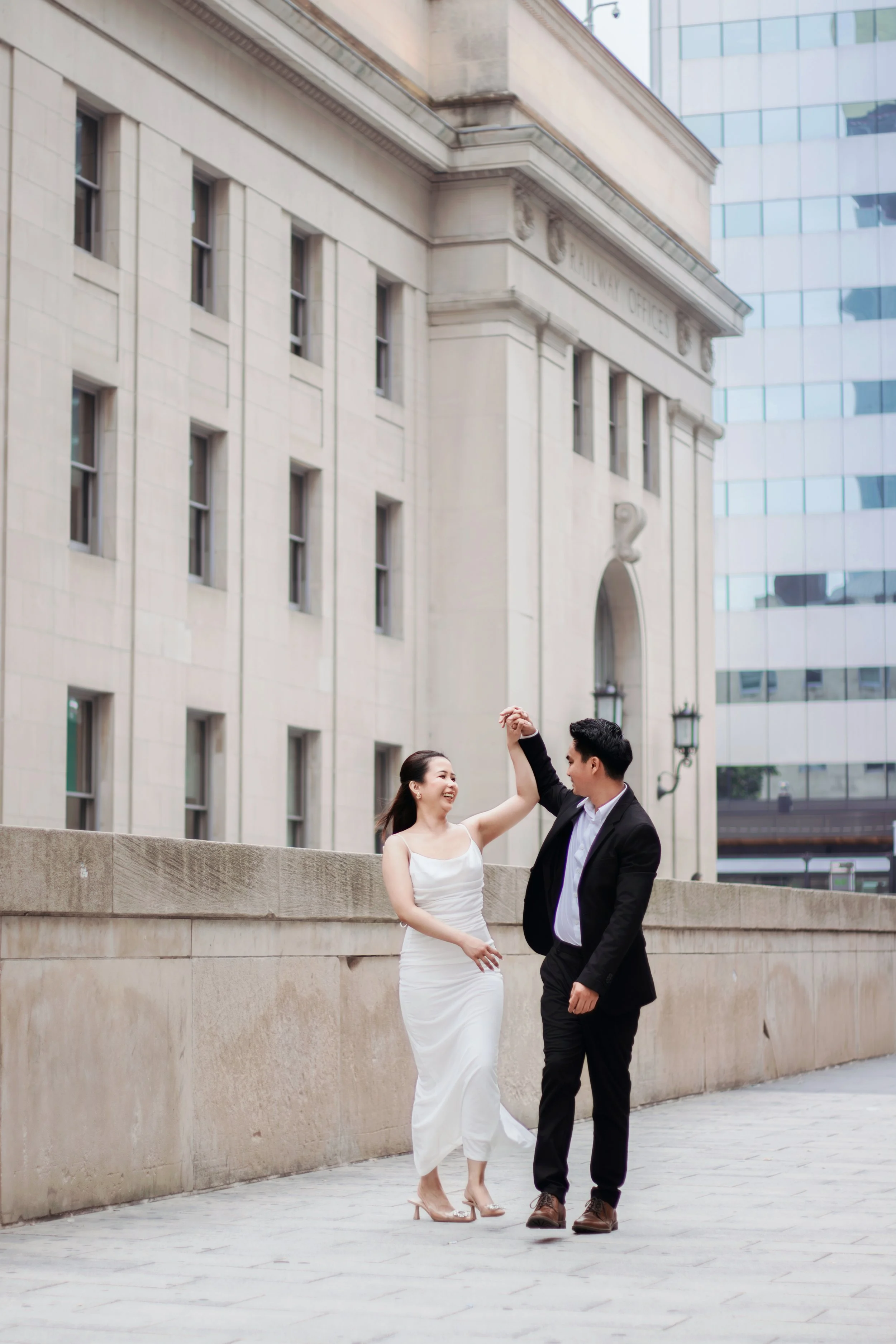 A couple dancing outside a building with a cityscape in the background.