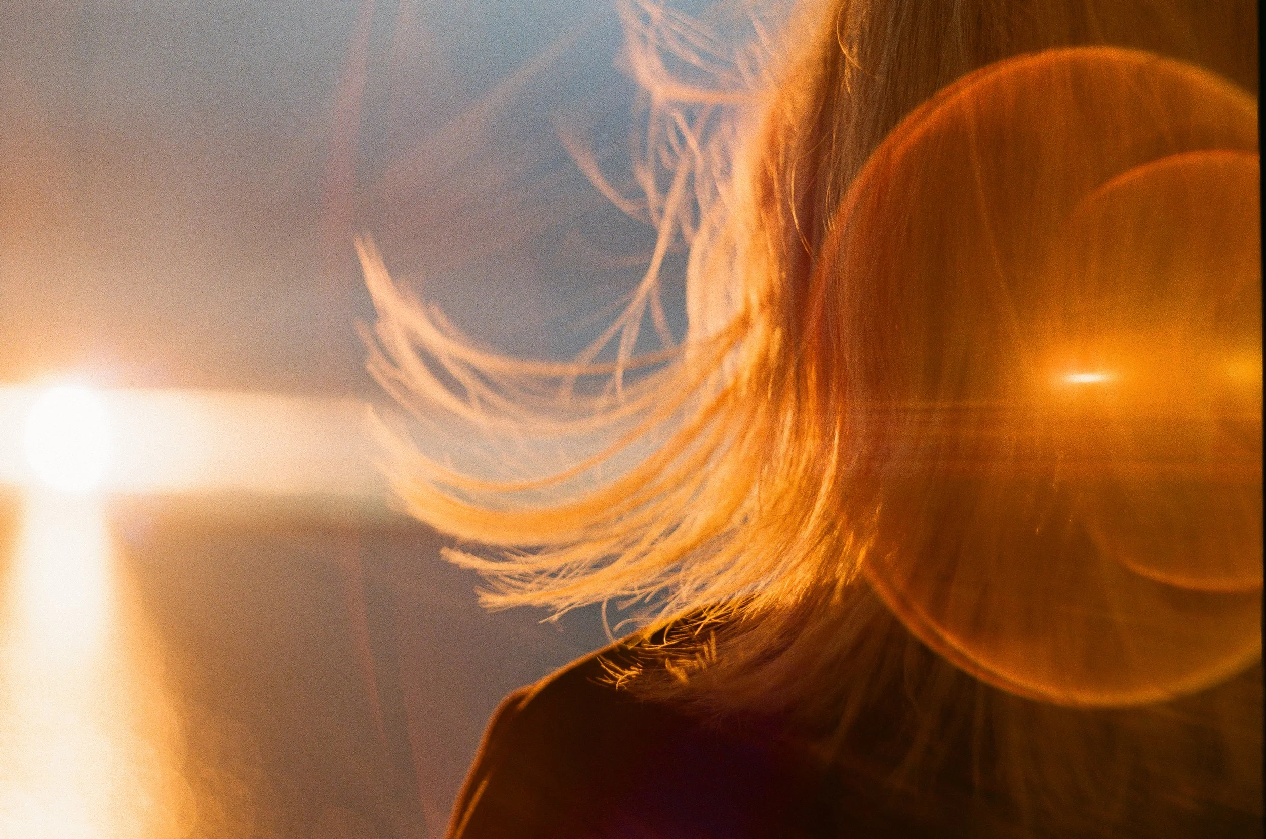 Close-up of a woman's face illuminated by a sunset, with her blond hair flowing and lens flare effects.