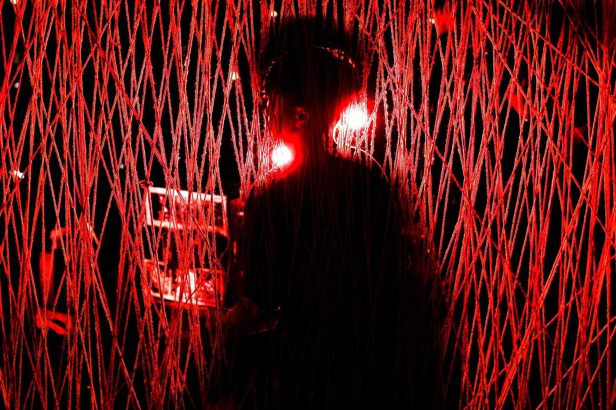 Person standing inside an art installation made of red neon lights and strings of lights, with a dark background.