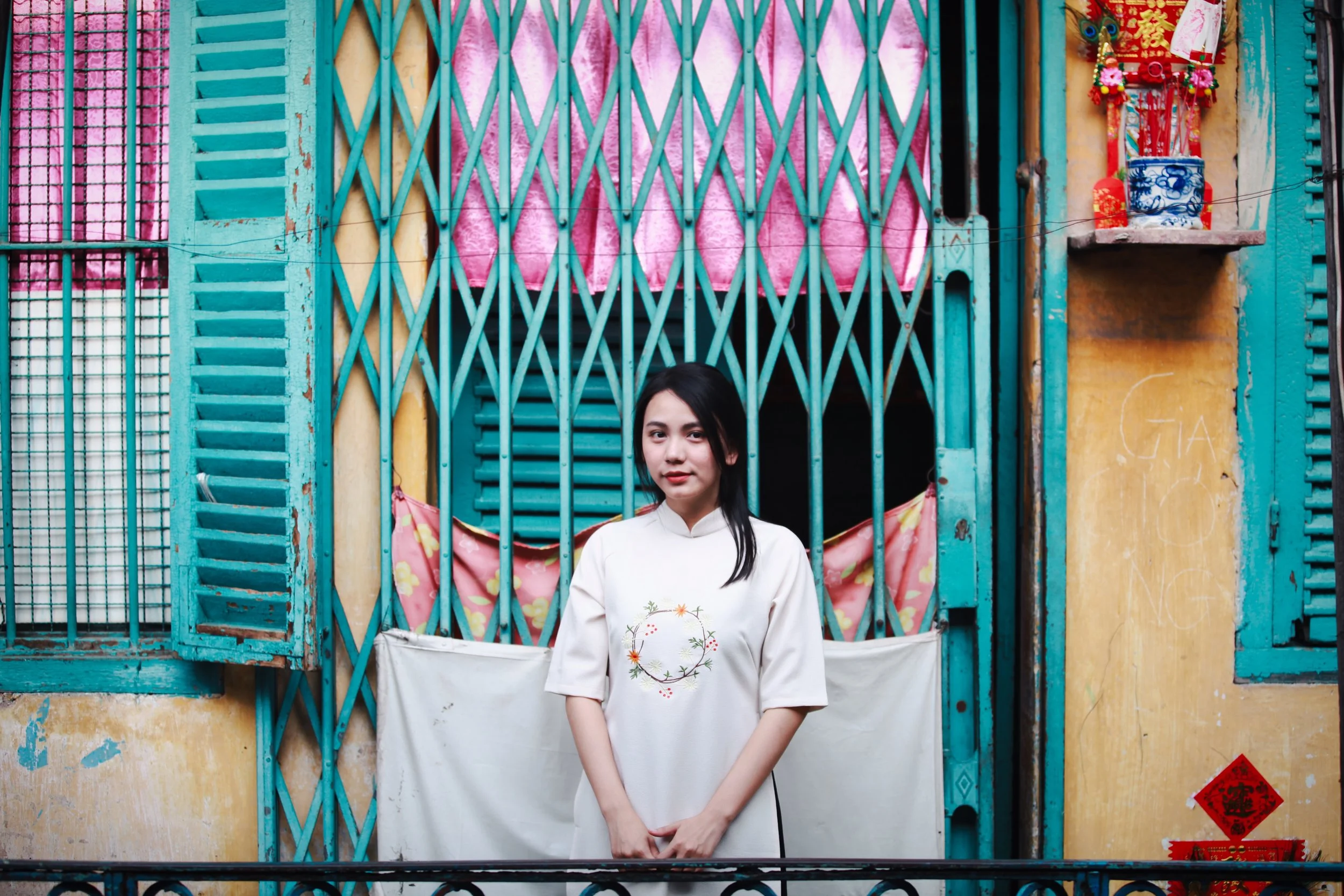 Young woman standing in front of a colorful, rustic building with turquoise shutters and traditional decorations.