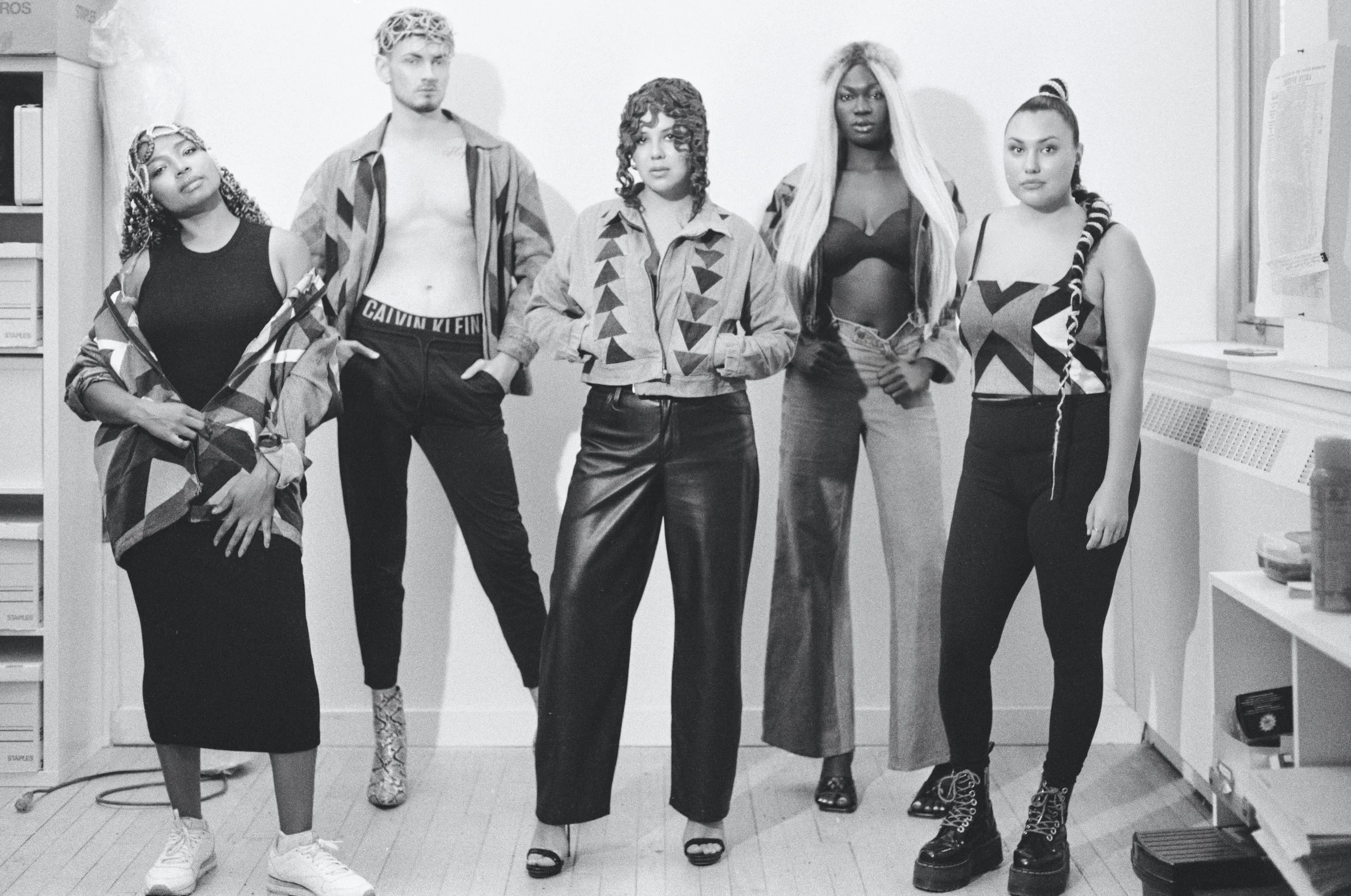 Group of five young women and one young man posing indoors, with diverse fashion styles and hairstyles, in black and white photo.
